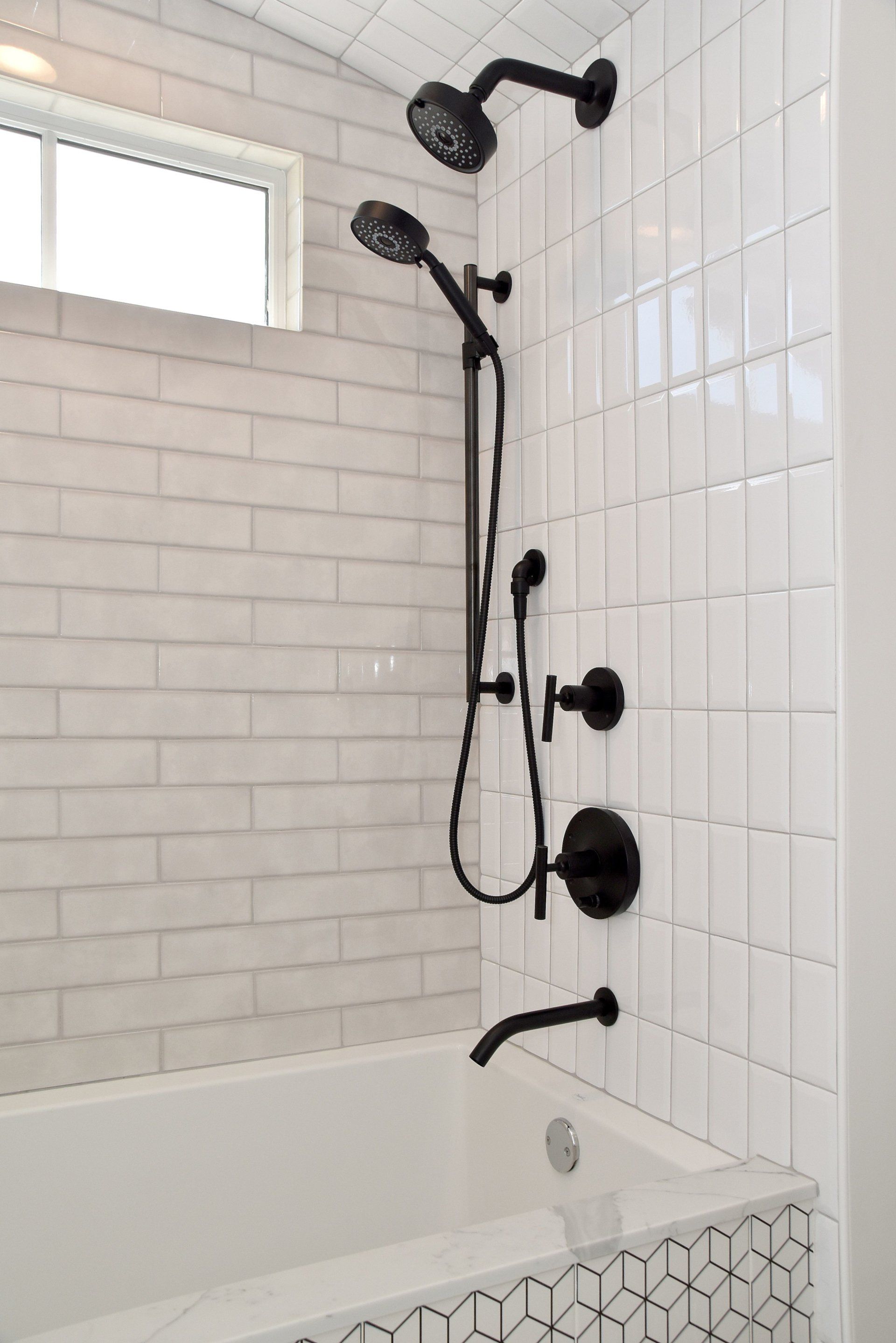A bathroom with white tiles , black shower heads and a bathtub.
