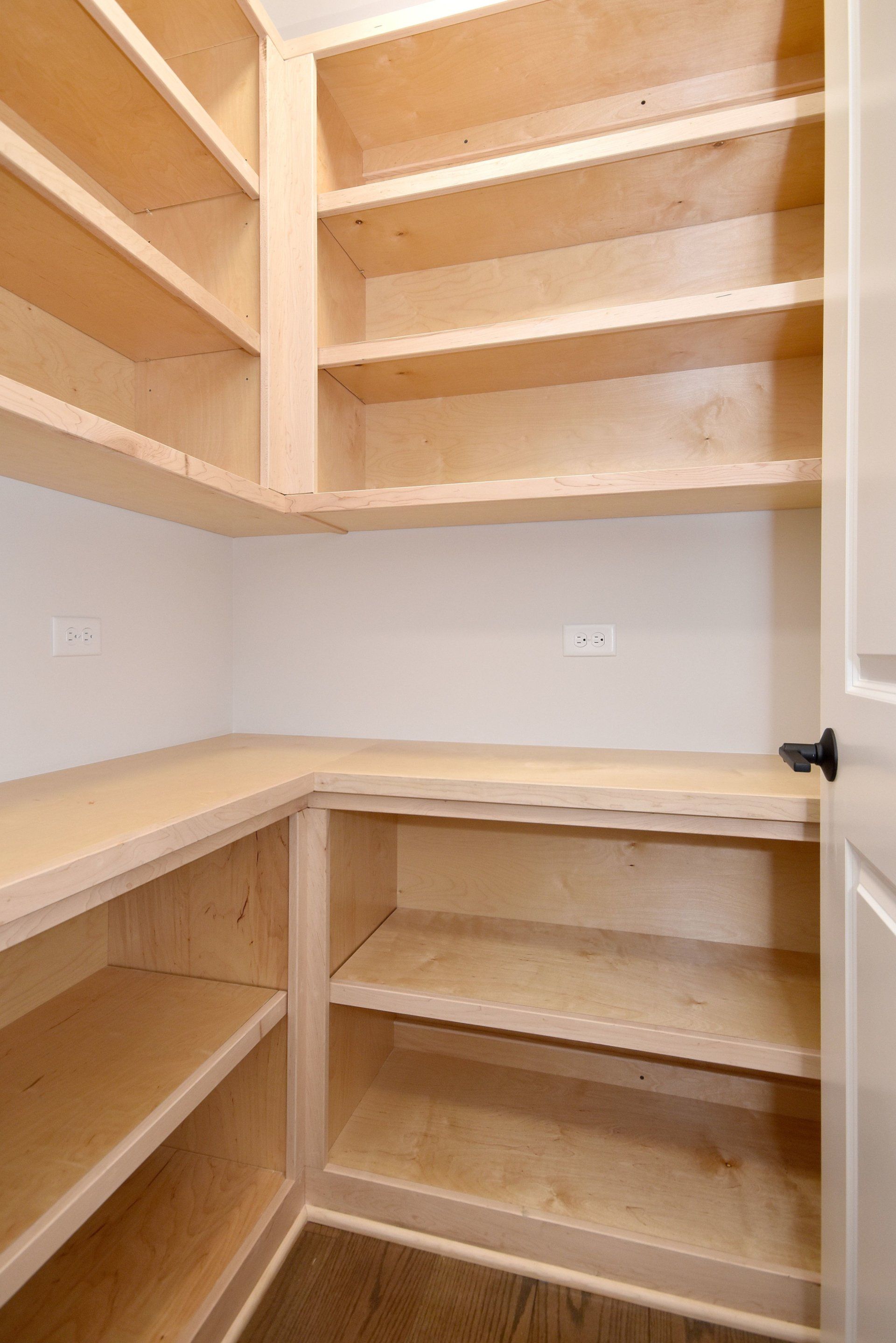 An empty pantry with wooden shelves and a white door.