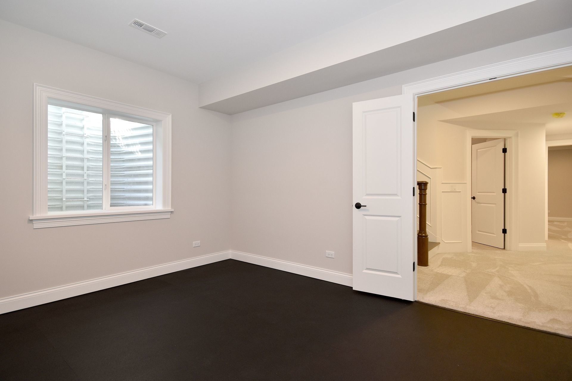 An empty basement with a window and black carpet.
