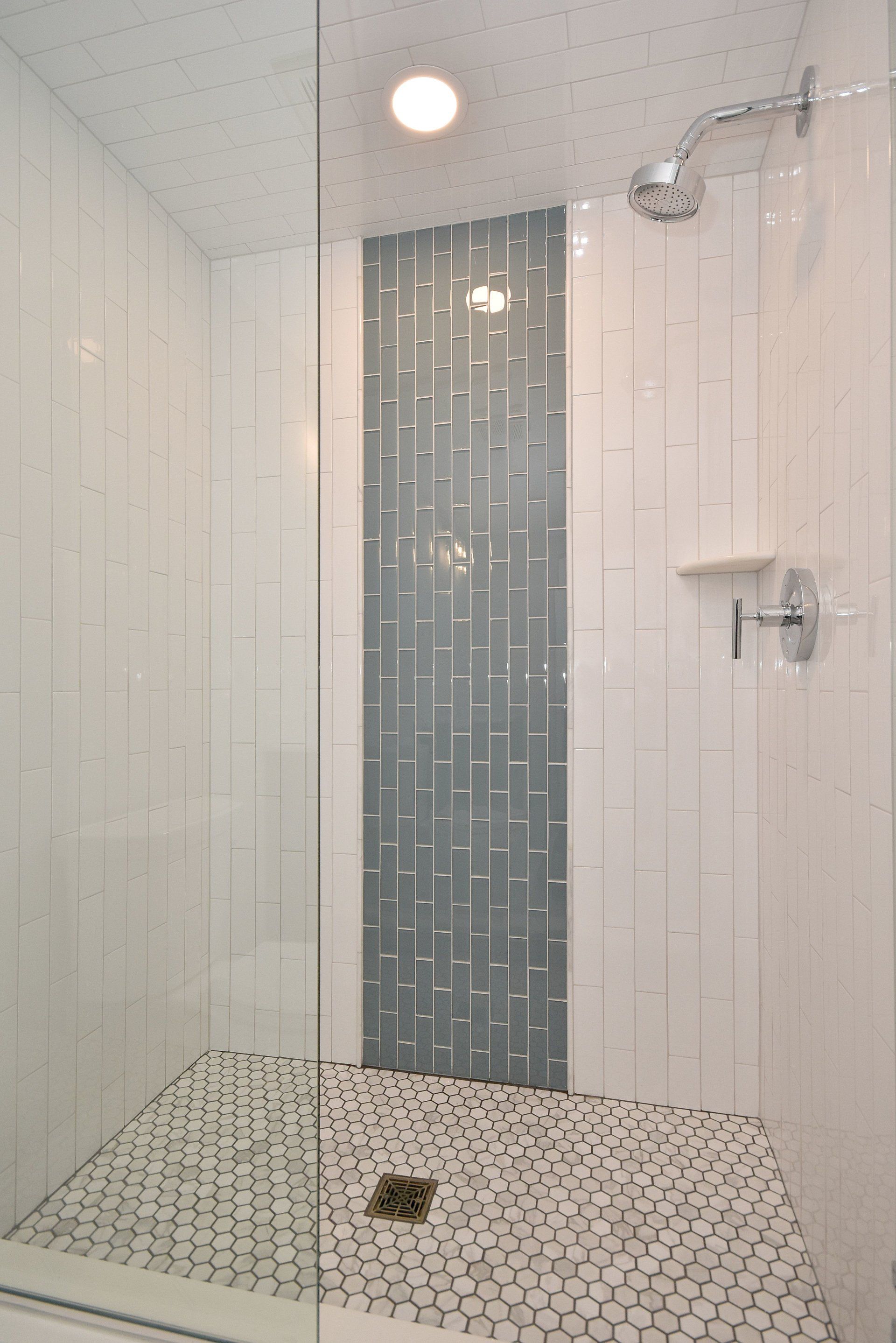 A walk in shower with white tiles and a shower head