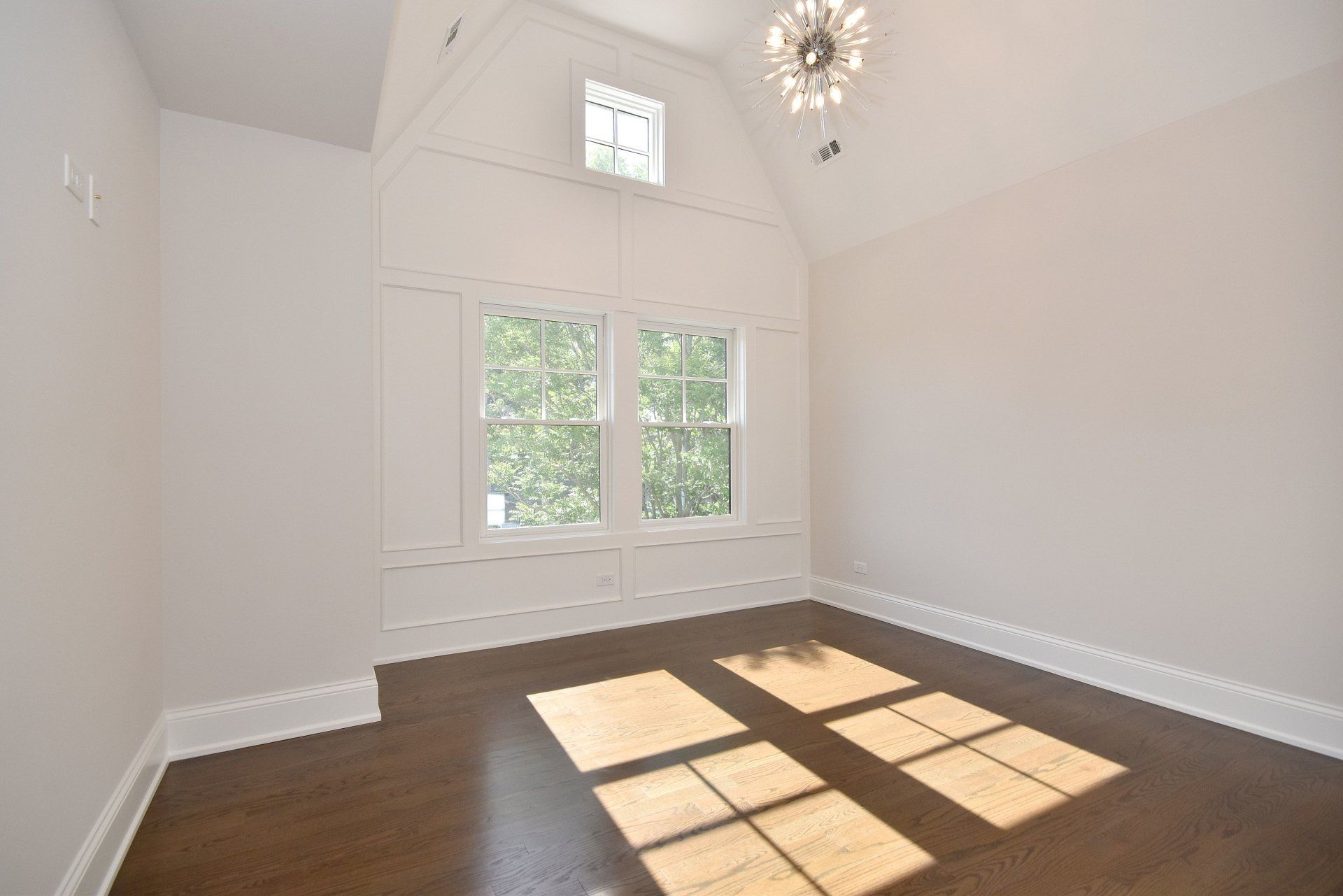 An empty room with hardwood floors and a chandelier hanging from the ceiling.
