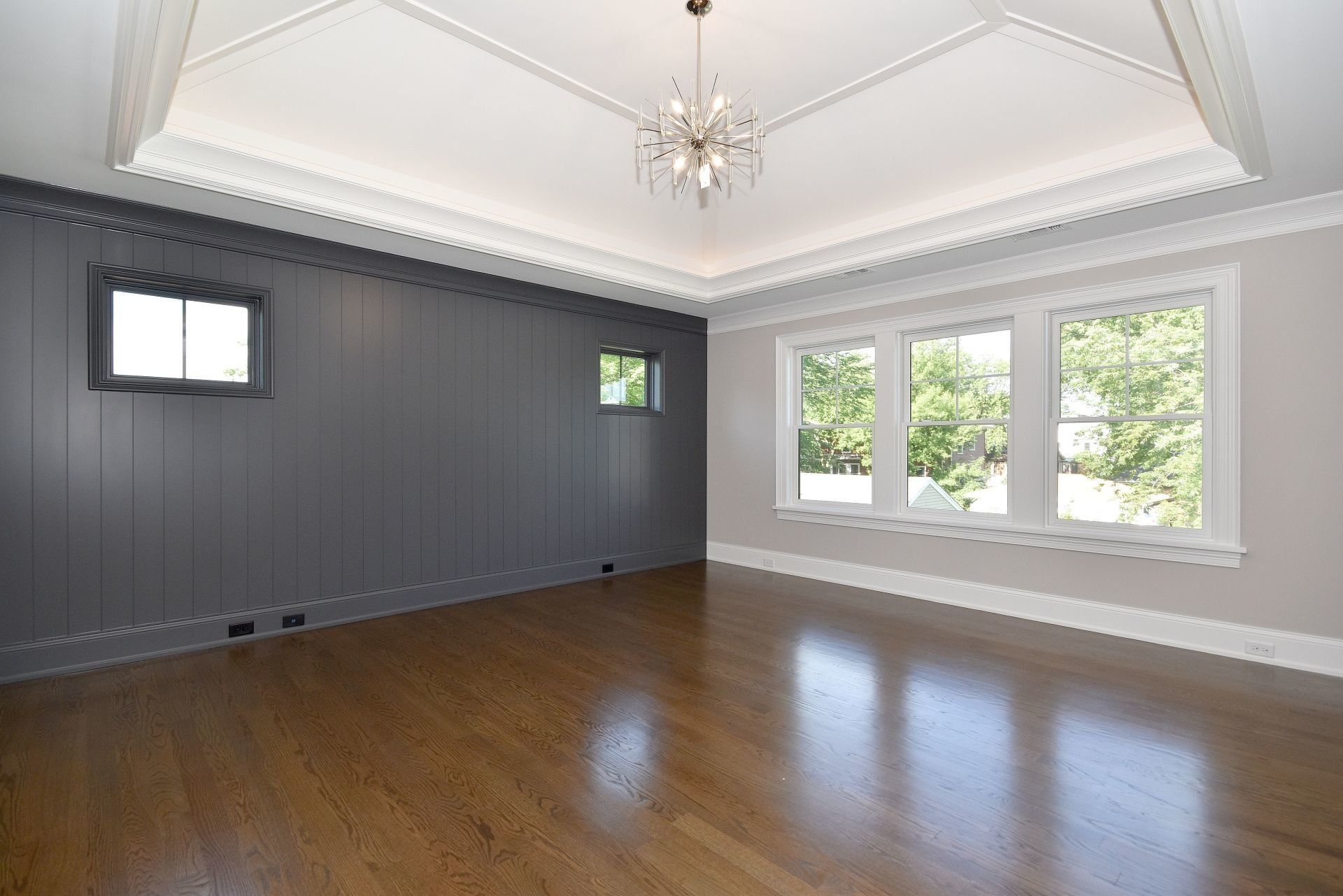 An empty living room with hardwood floors and a chandelier hanging from the ceiling.