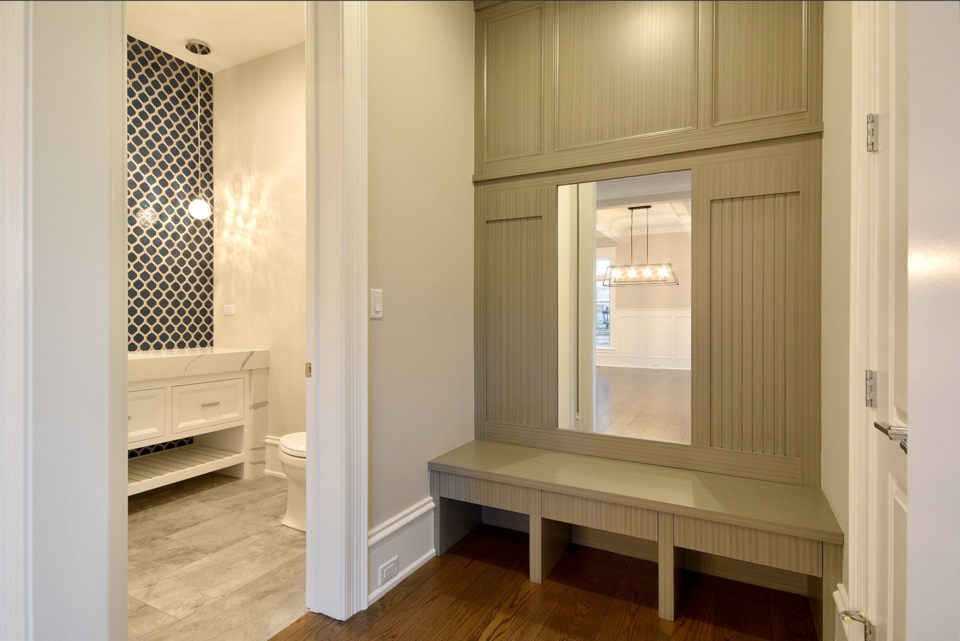 A hallway with a bench and a mirror leading to a bathroom.