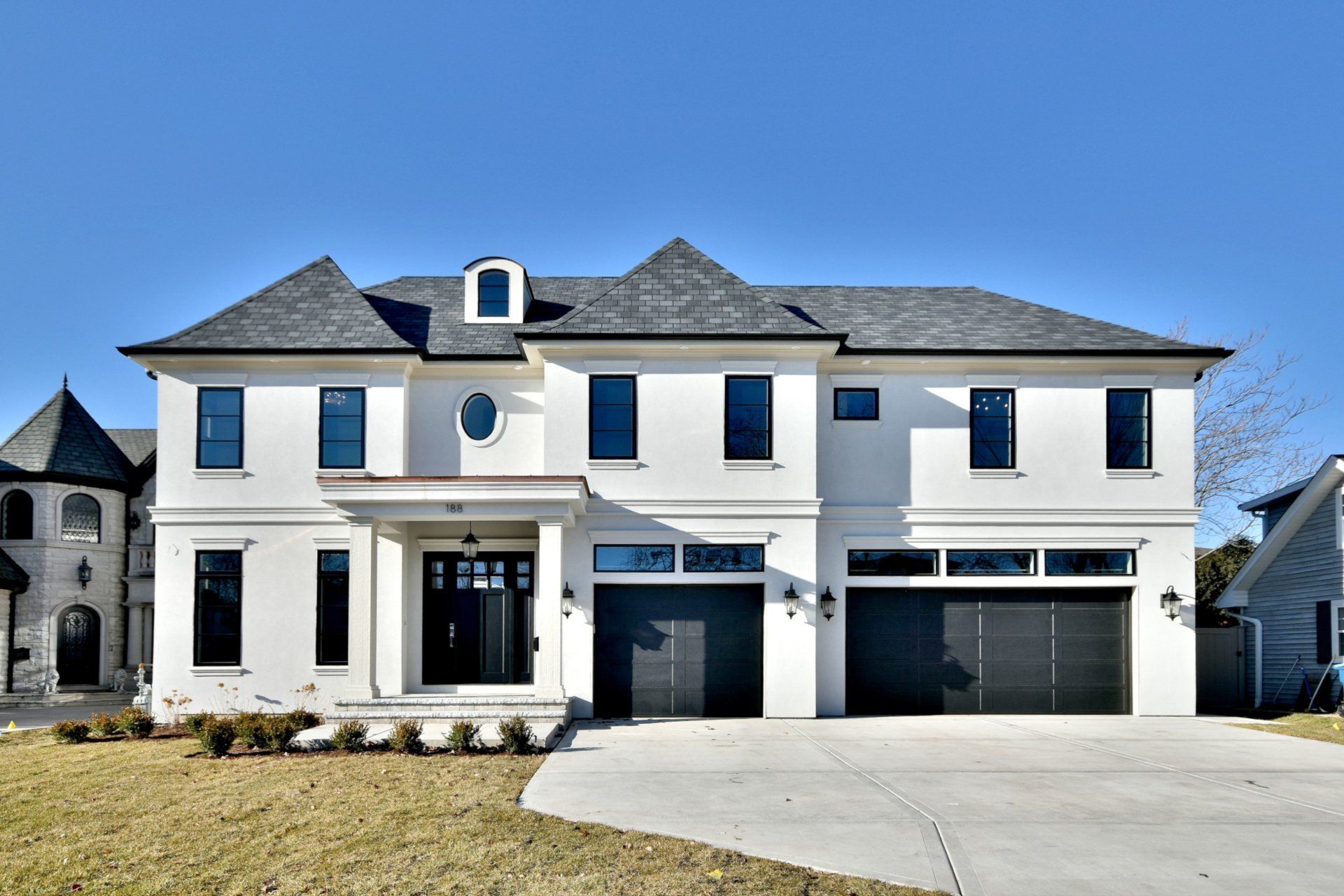 A large white house with a gray roof and black garage doors.