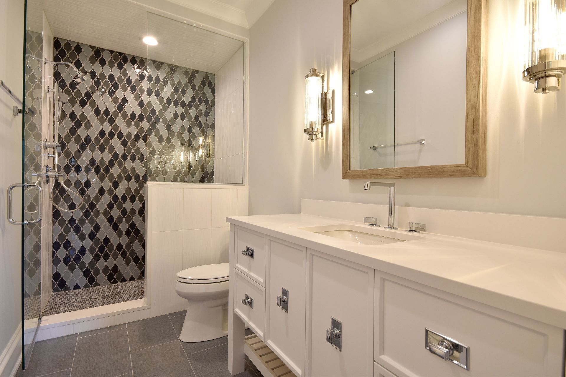 A bathroom with a toilet , sink , mirror and walk in shower.