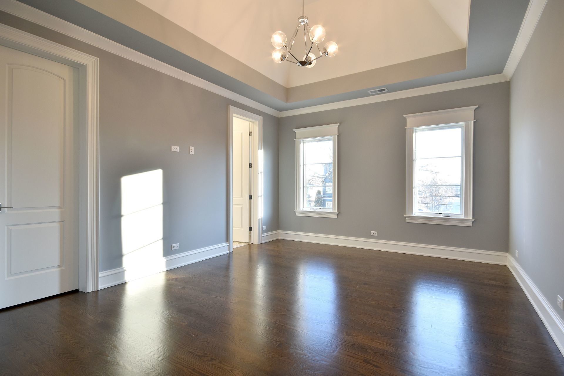 A large empty room with hardwood floors and a chandelier hanging from the ceiling.
