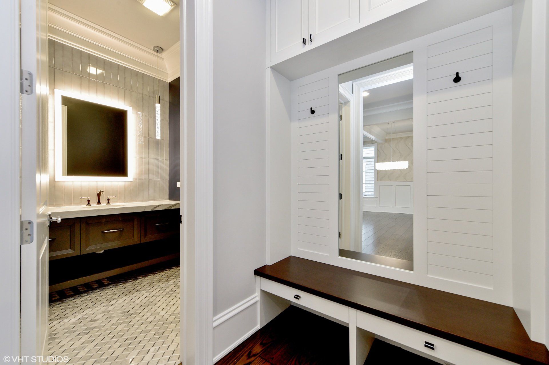 A hallway with a bench and a mirror leading to a bathroom.