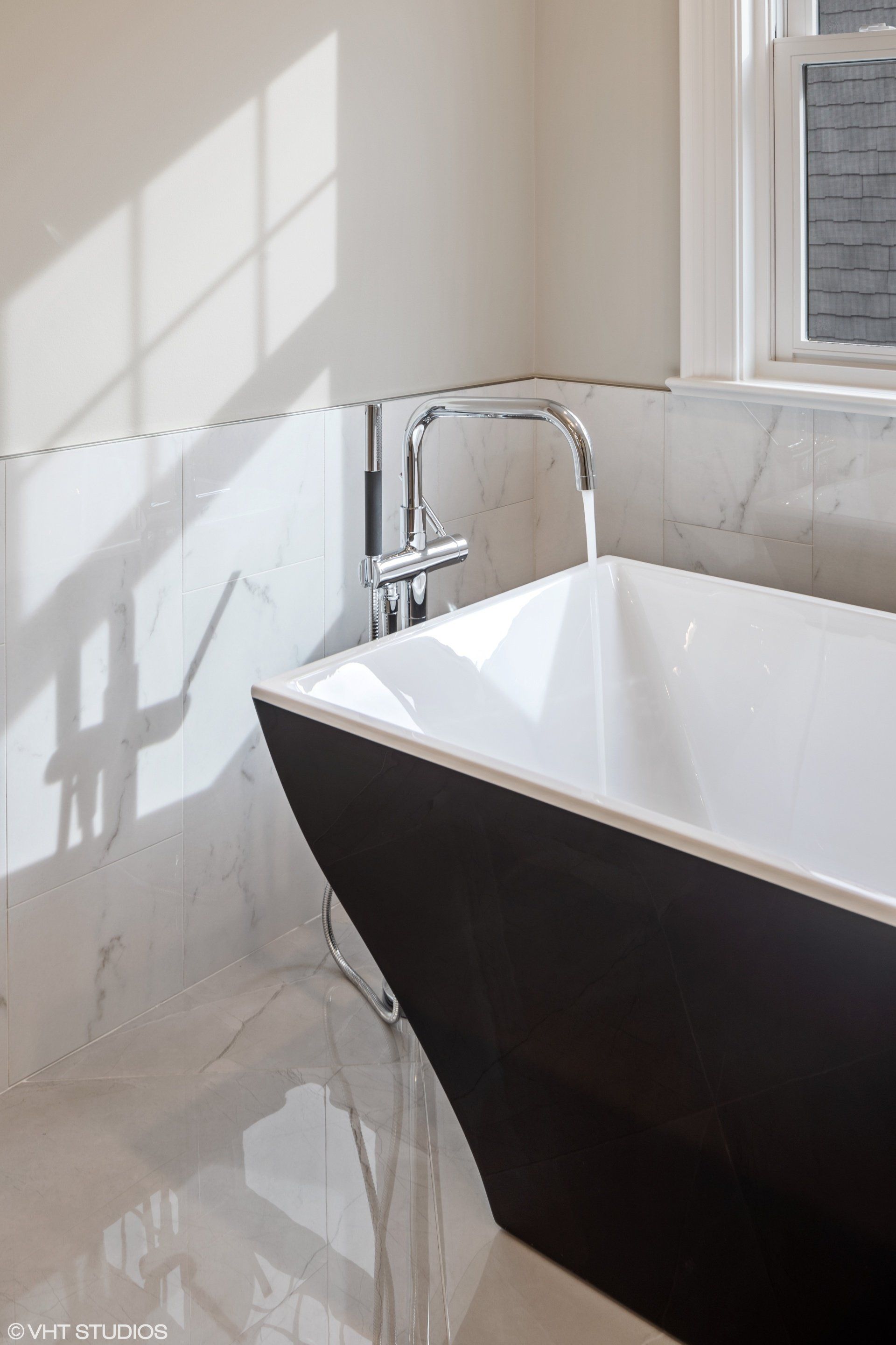 A black and white bathtub is in a bathroom next to a window.