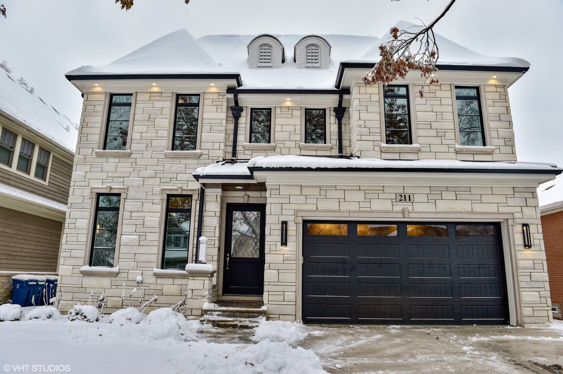 A large brick house with a black garage door is covered in snow.