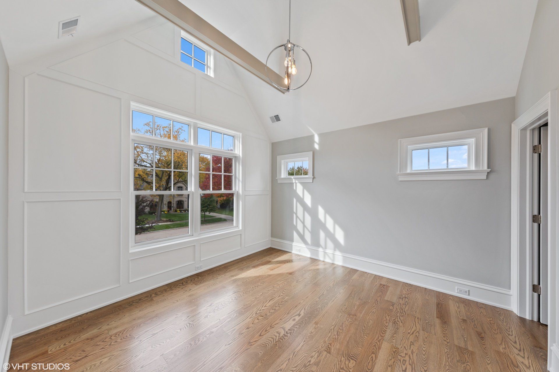 An empty room with hardwood floors and a vaulted ceiling.