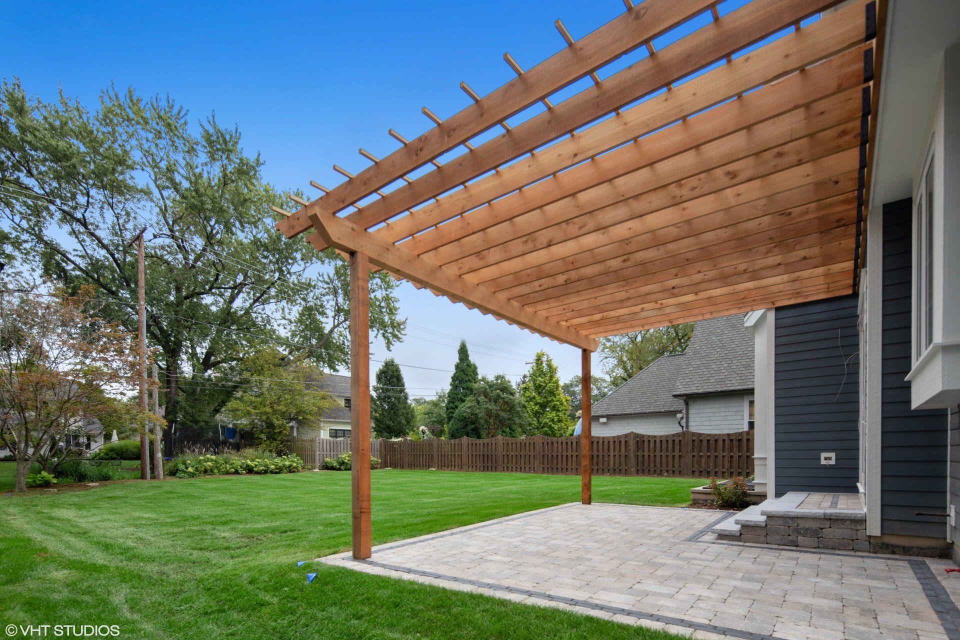 There is a wooden pergola in the backyard of a house.