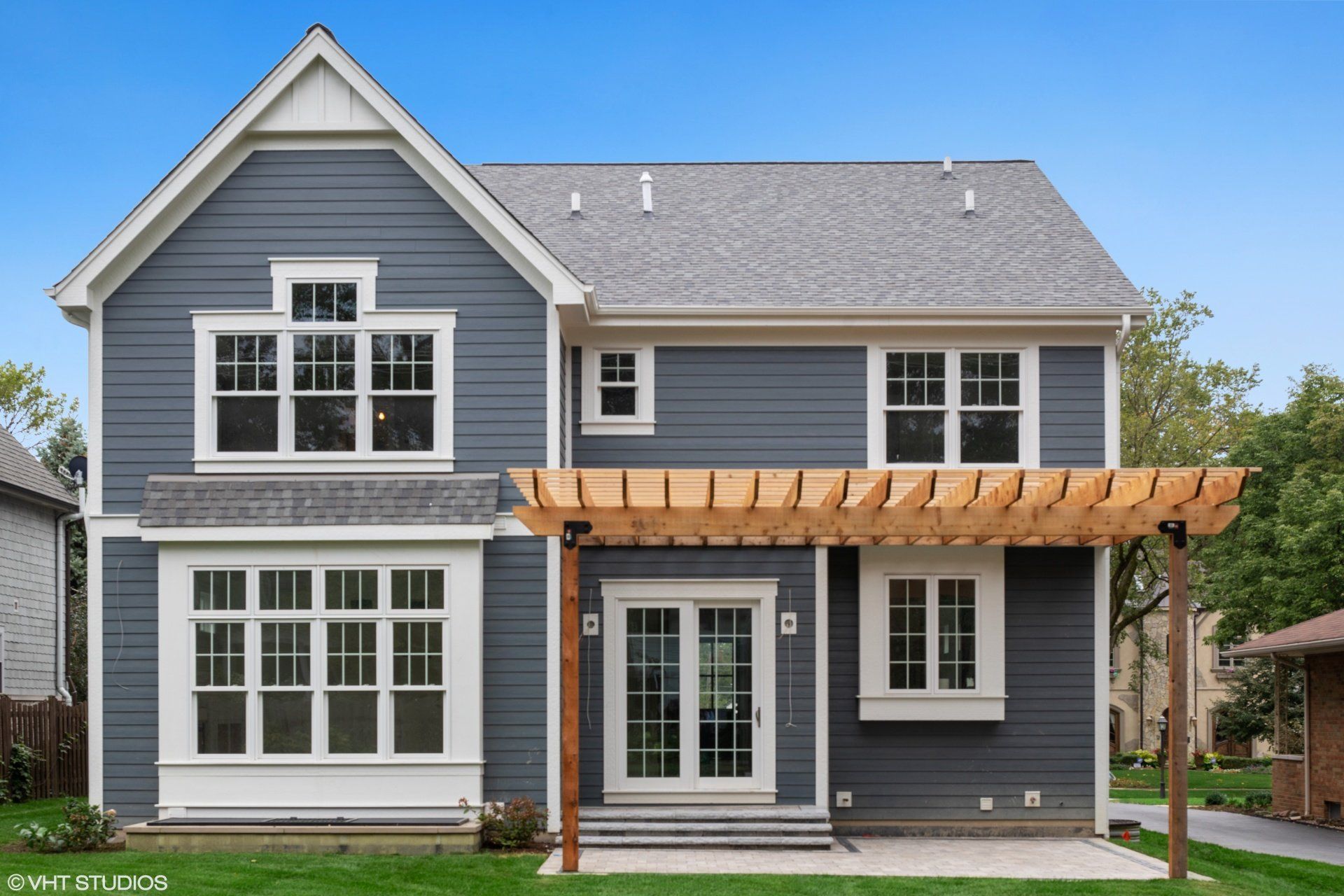 A gray house with white trim and a pergola on the backyard