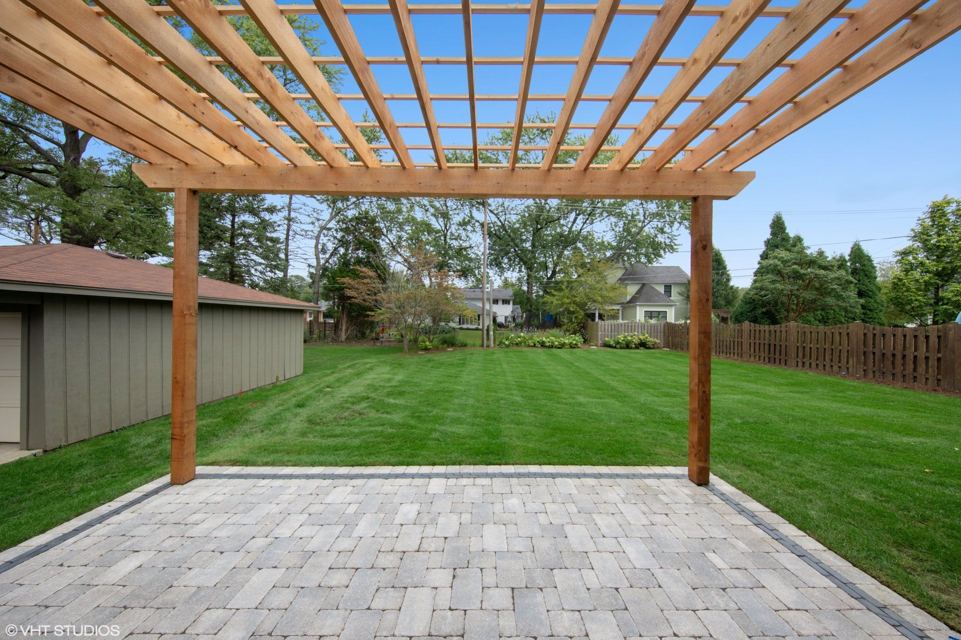 A patio with a pergola overlooking a lush green yard