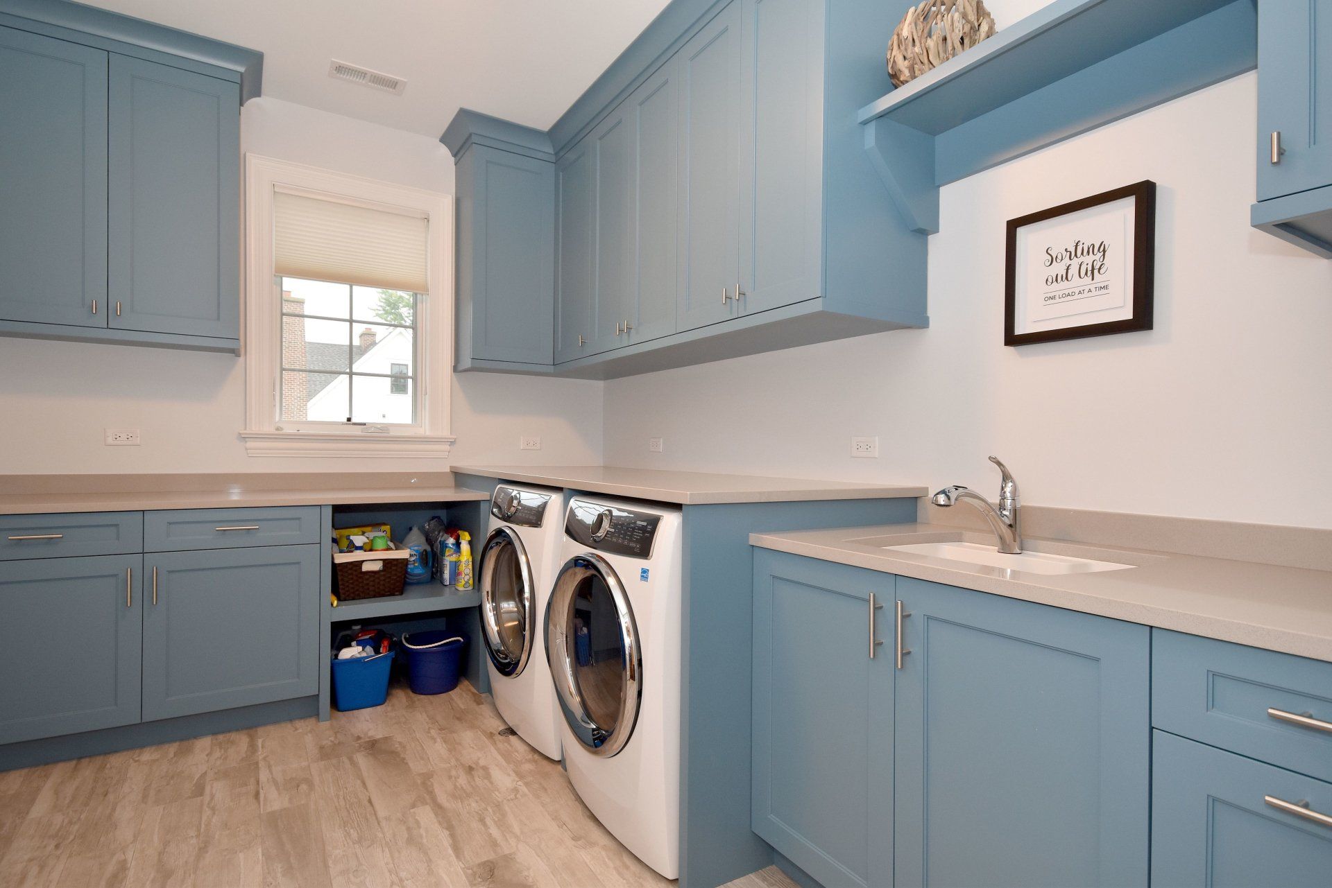 A laundry room with blue cabinets , a washer and dryer , and a sink.