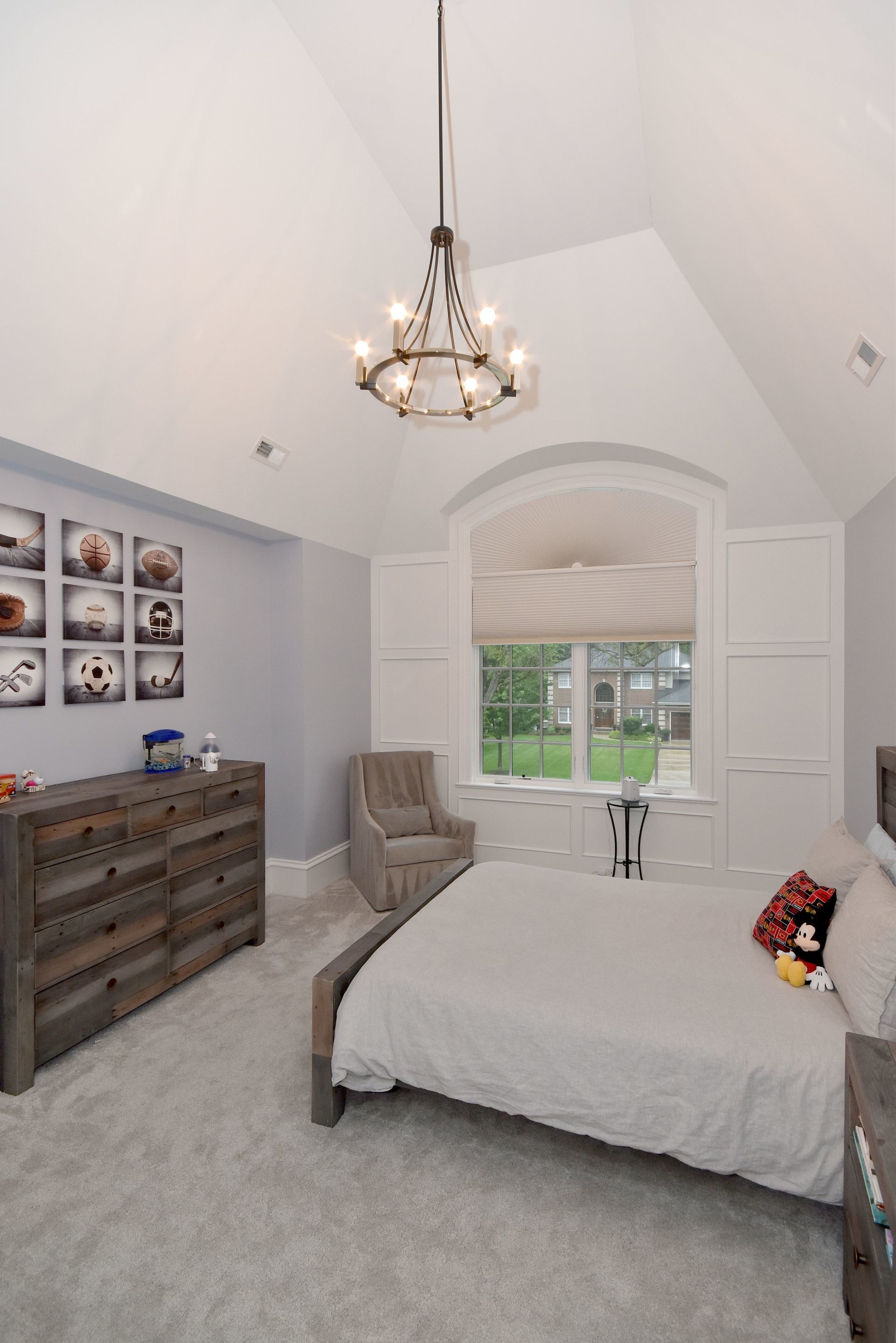 A bedroom with a bed , dresser , chair and chandelier.
