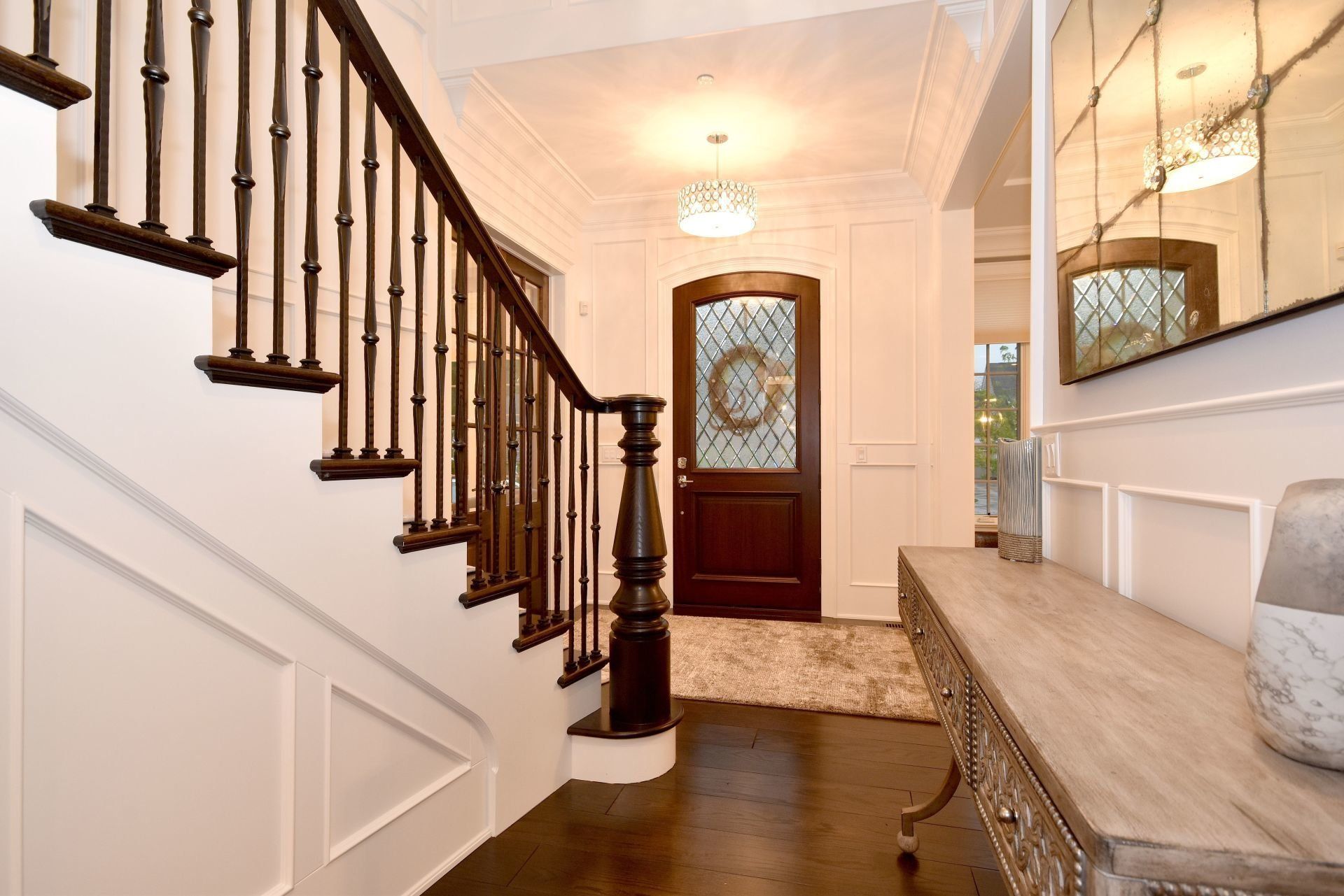 A hallway with stairs , a table and a mirror.
