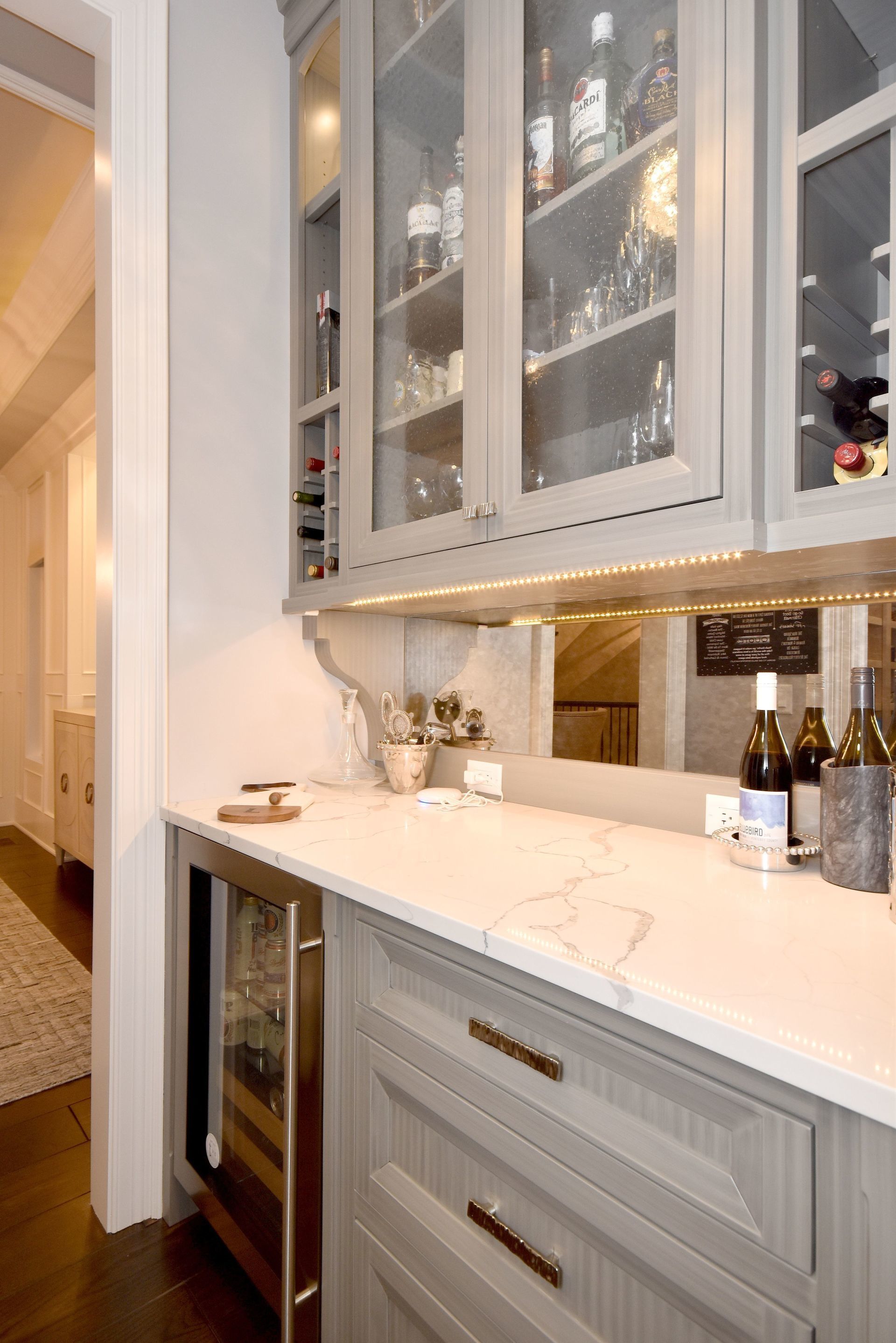A kitchen with a wine cooler , bottles of wine , and glasses on the counter.