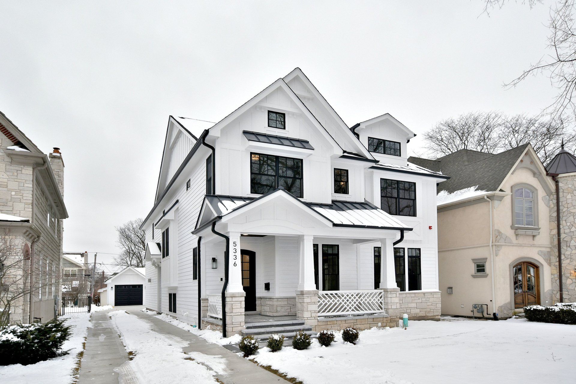 A large white house with black windows is surrounded by snow.