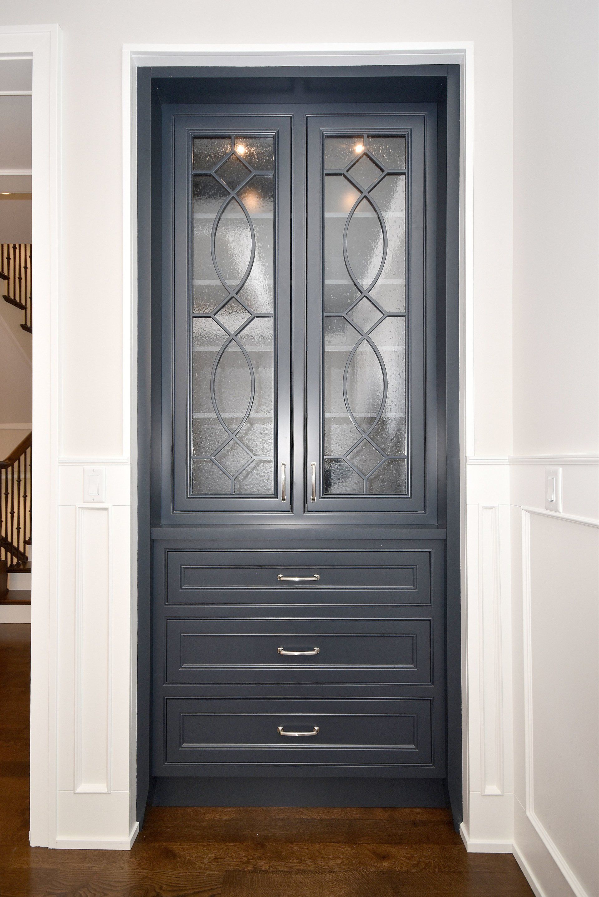 A black cabinet with drawers and a glass door in a hallway.