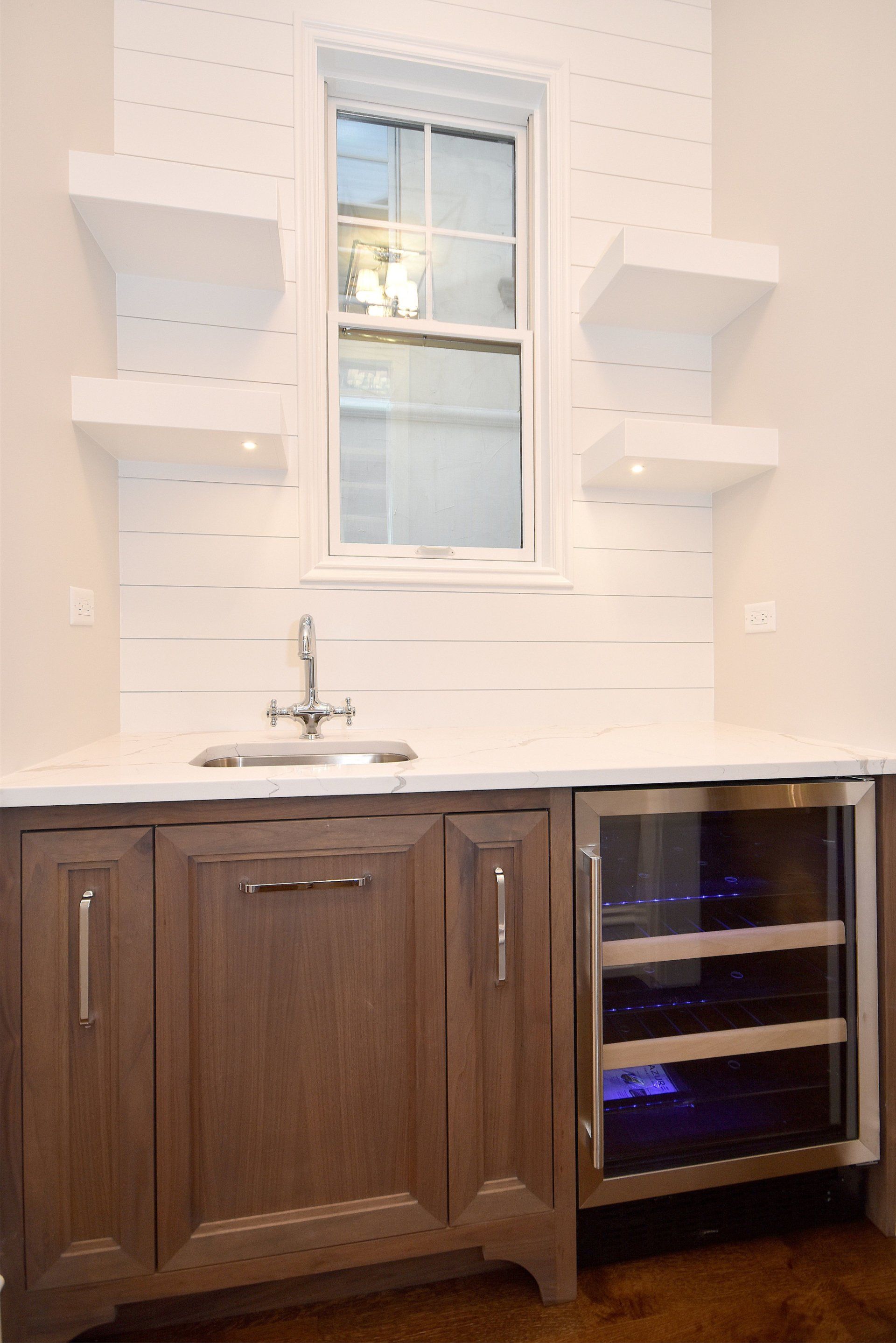 A kitchen with a sink , refrigerator , shelves and a window.