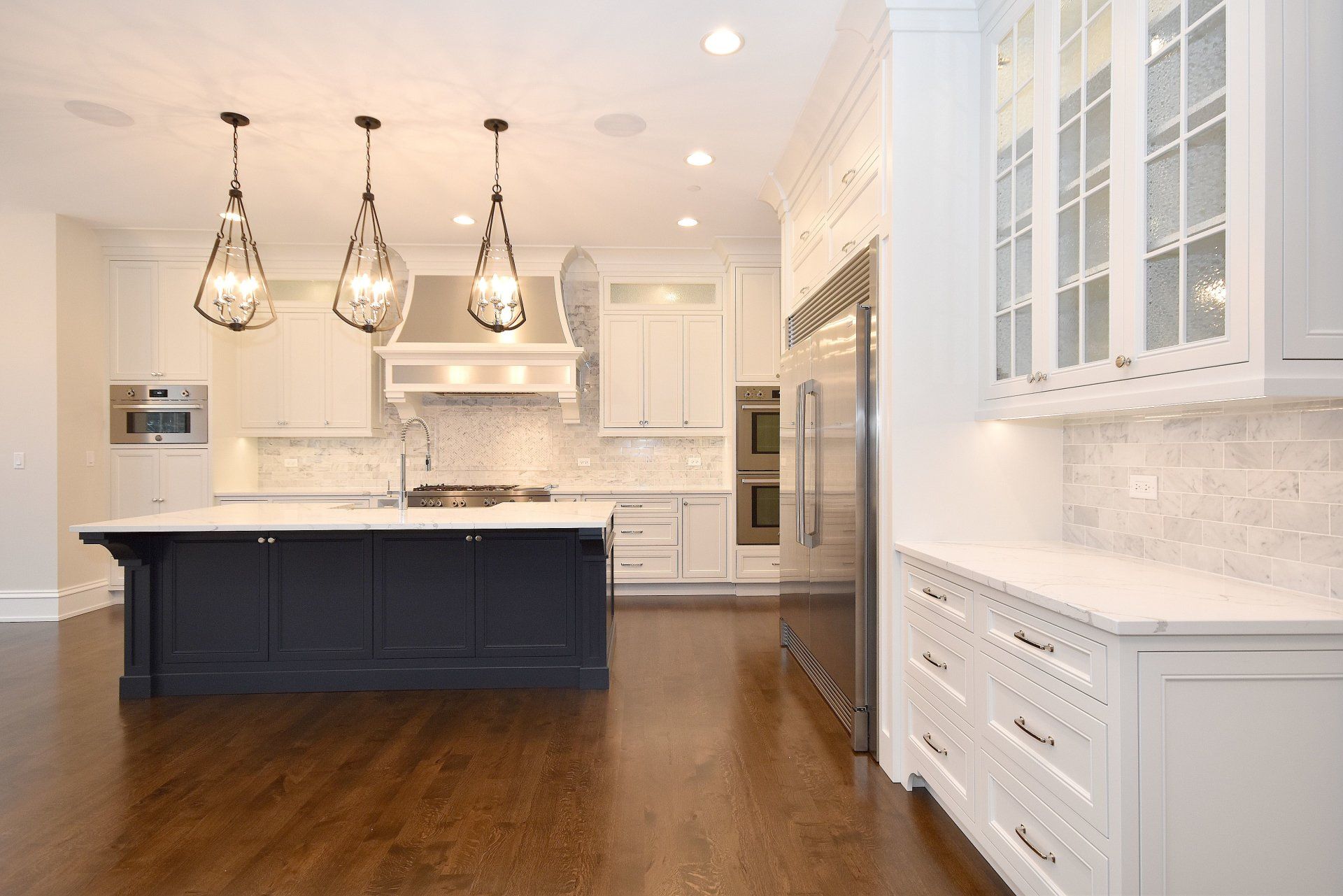 A kitchen with white cabinets , stainless steel appliances , a large island , and hardwood floors.