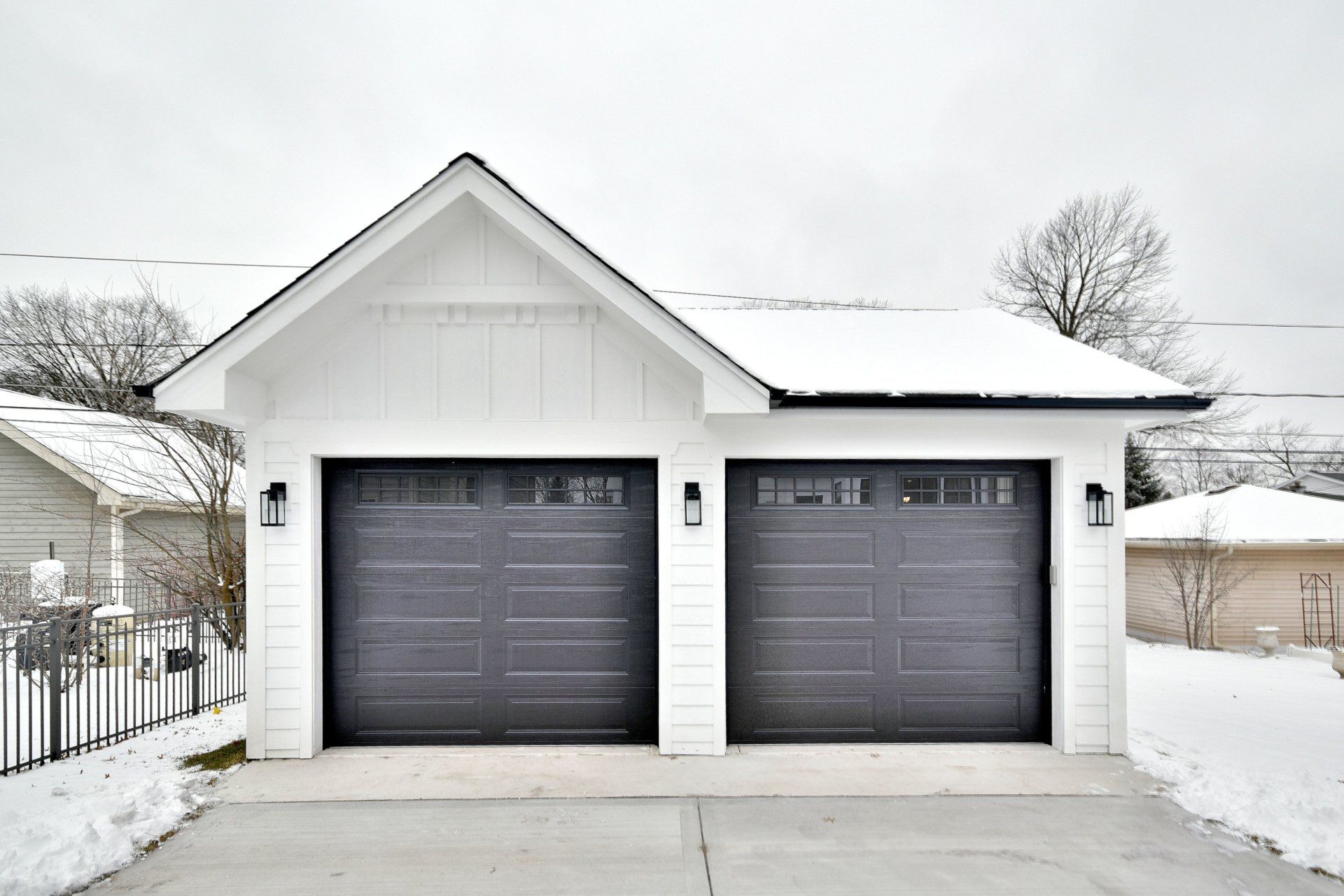 A white garage with black garage doors is covered in snow.