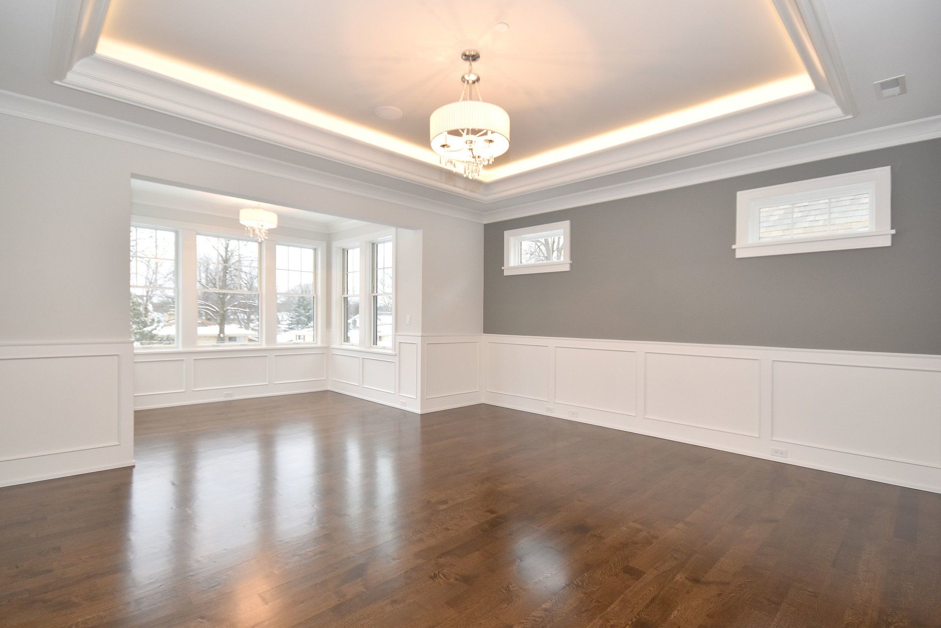 An empty living room with hardwood floors and a chandelier.
