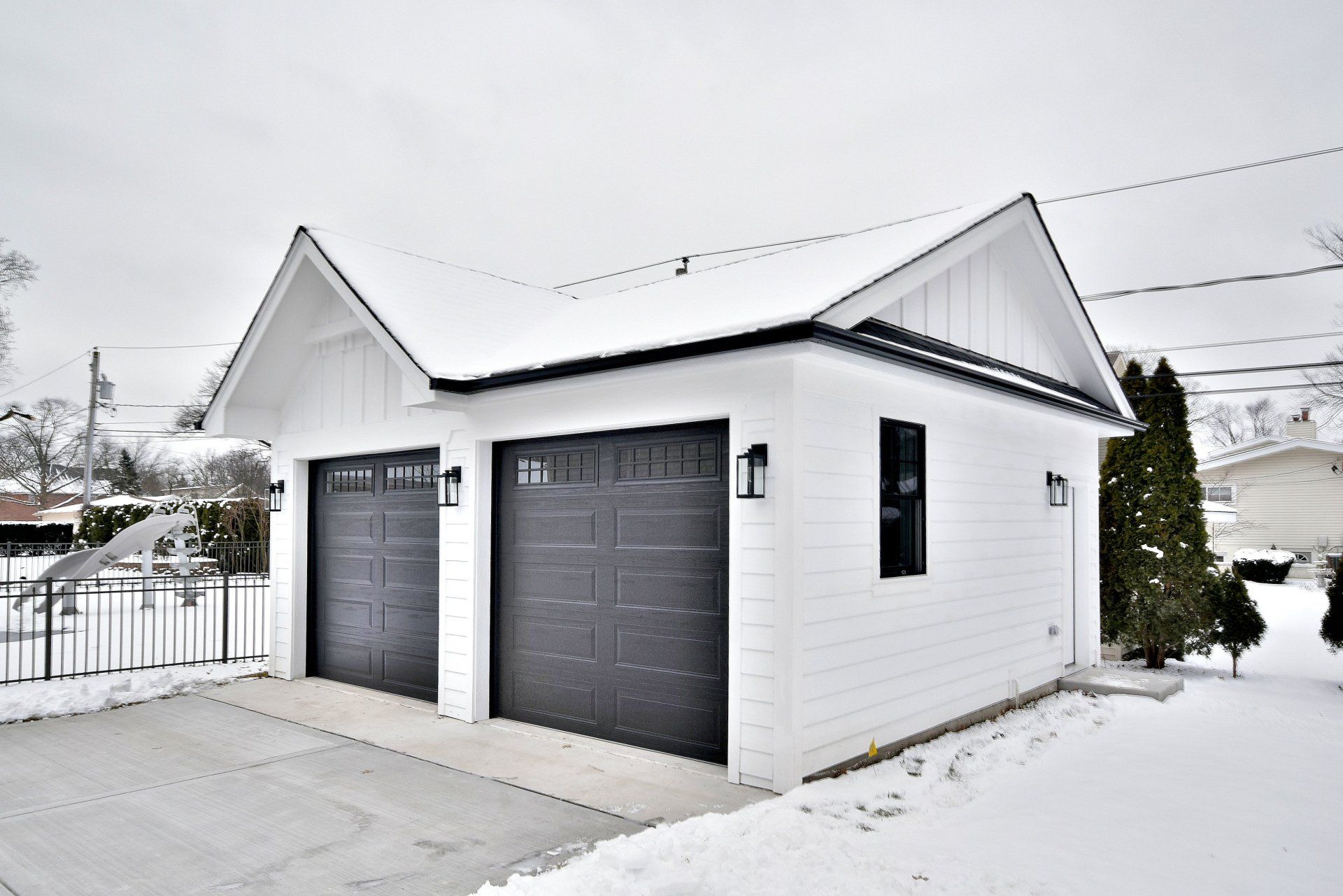 A white garage with black garage doors is covered in snow.