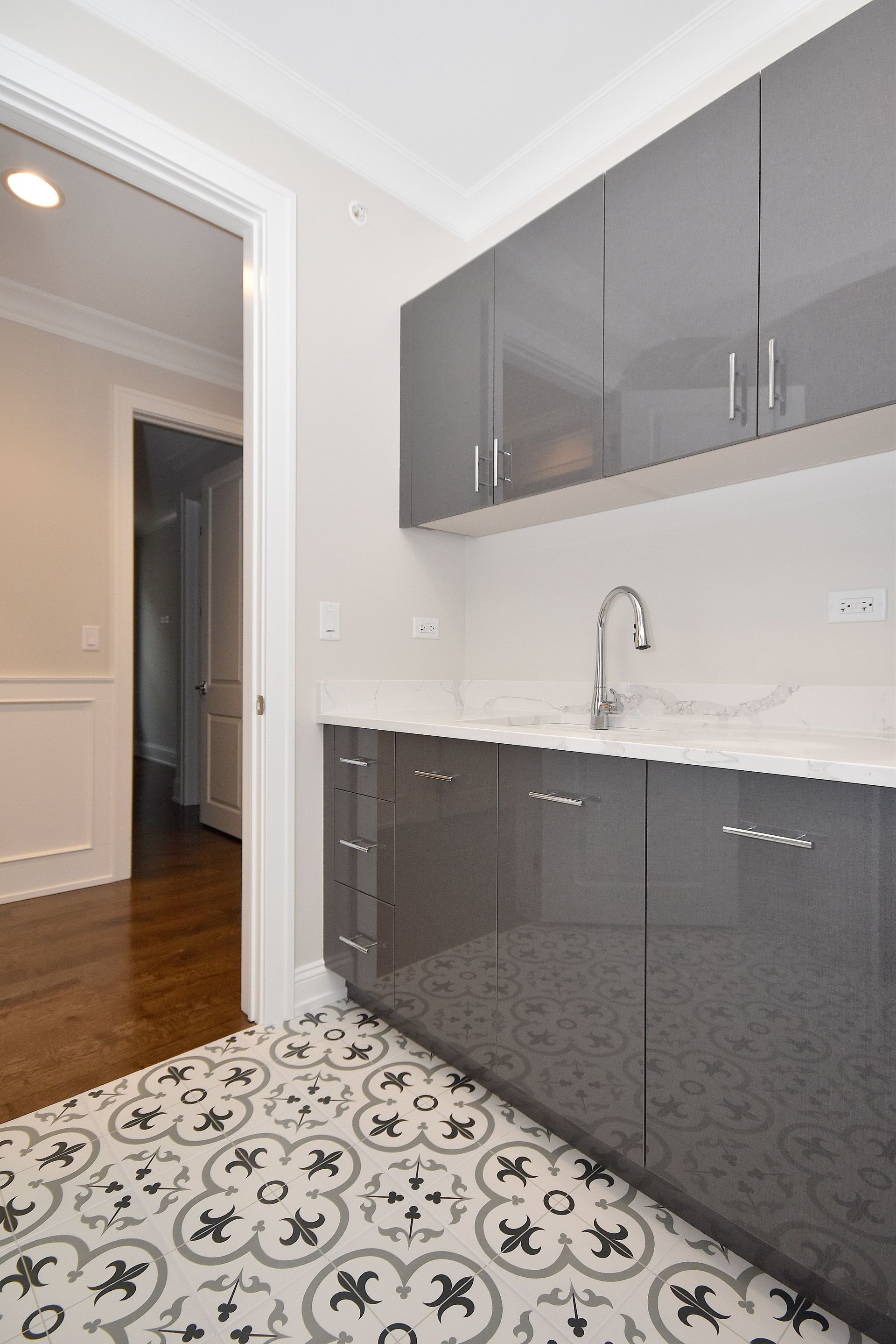A kitchen with gray cabinets , white counter tops , and a sink.