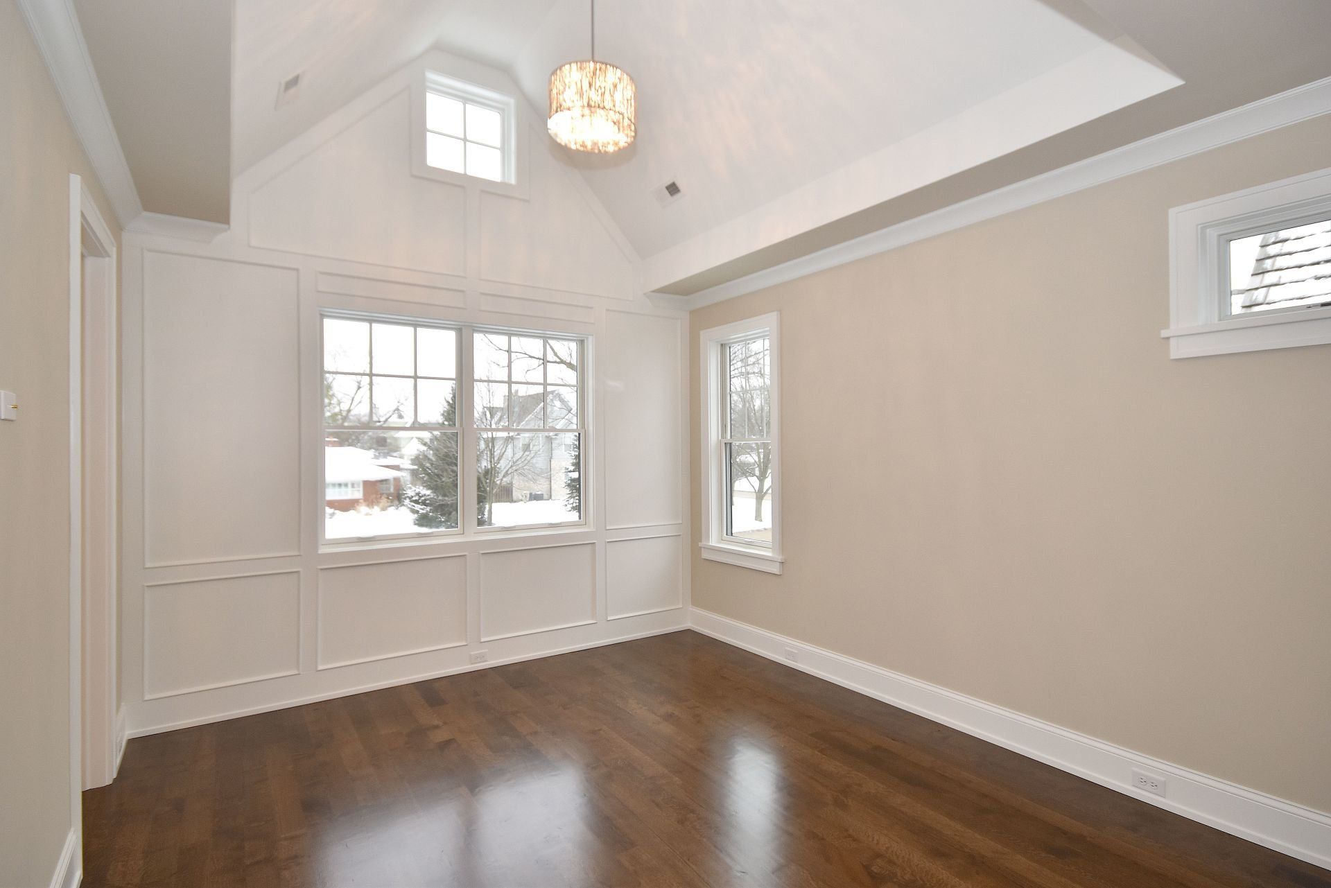An empty room with hardwood floors and a vaulted ceiling.