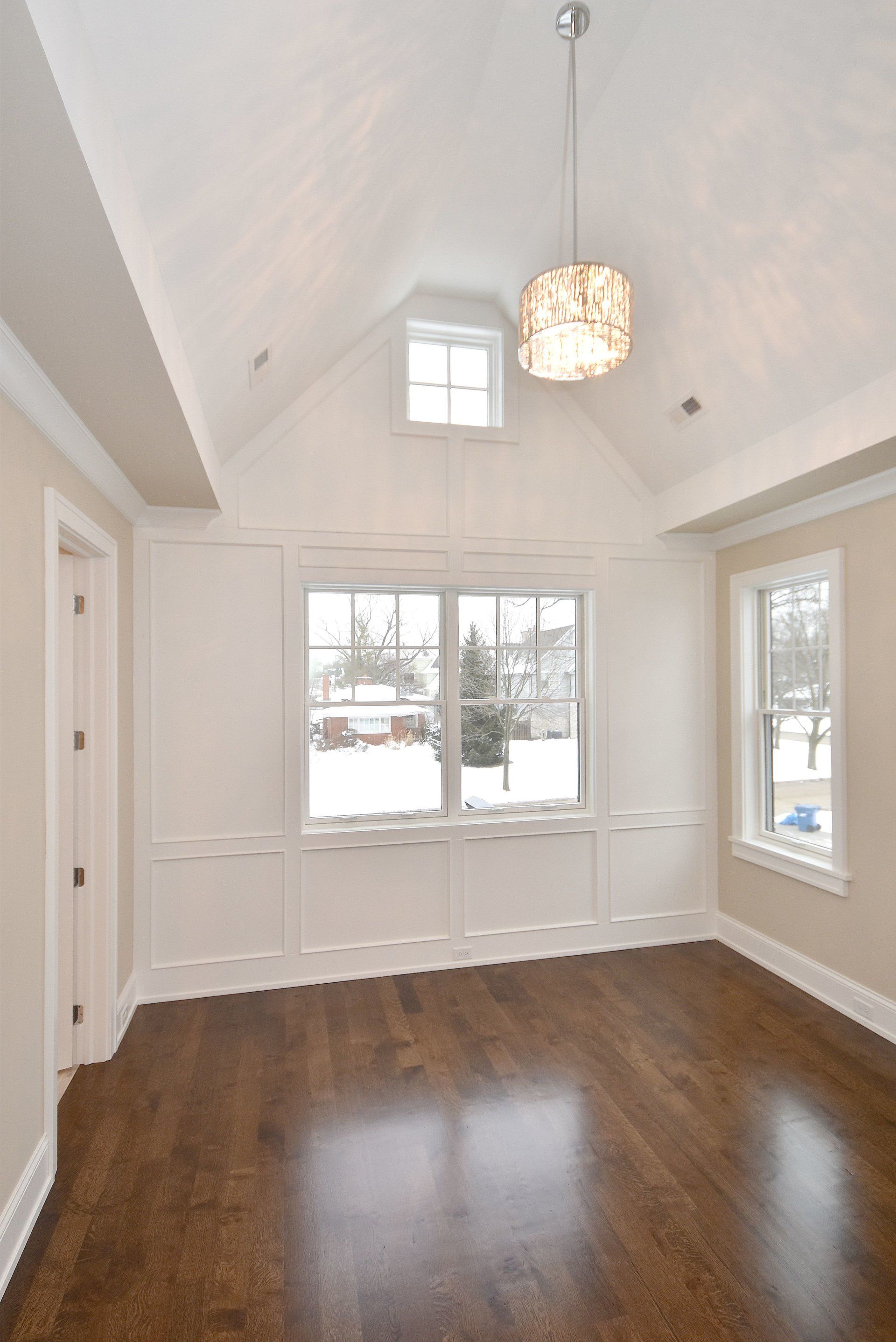 An empty room with hardwood floors and a vaulted ceiling.