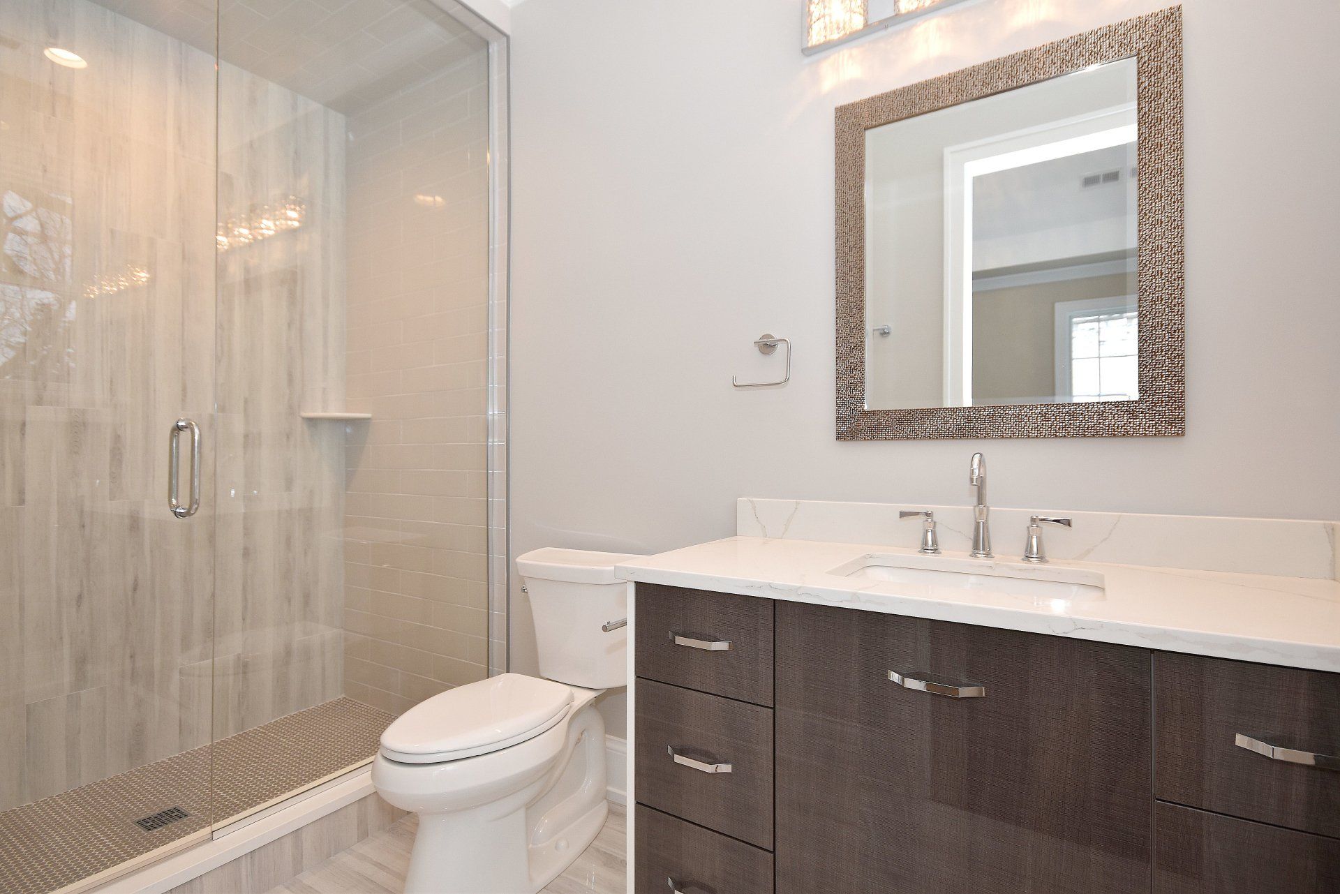 A bathroom with a toilet , sink , mirror and walk in shower.