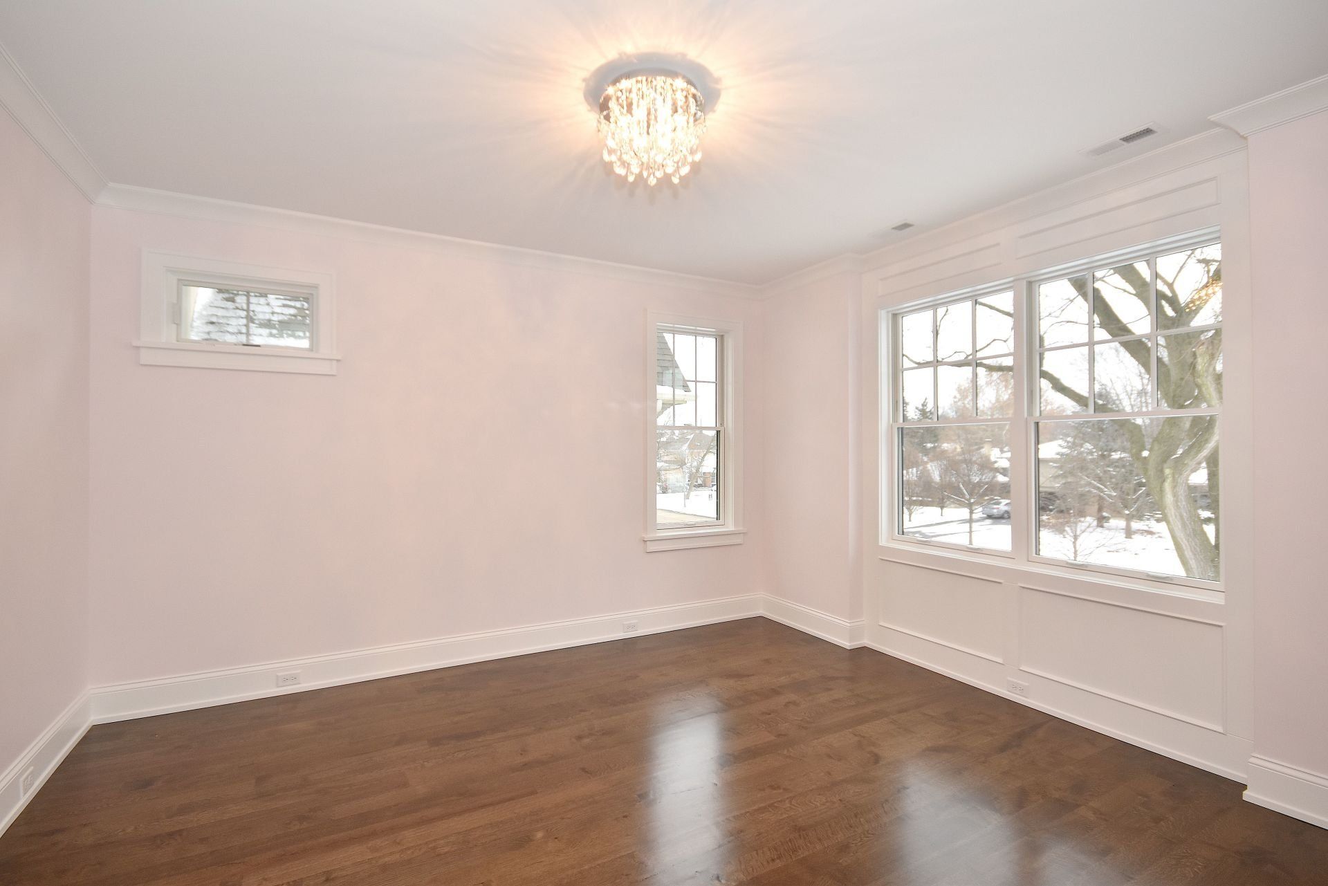 An empty room with hardwood floors and a chandelier.