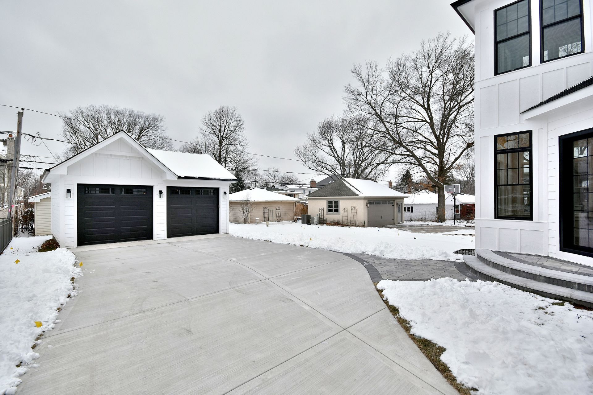 A snowy driveway leading to a white house with two garages.