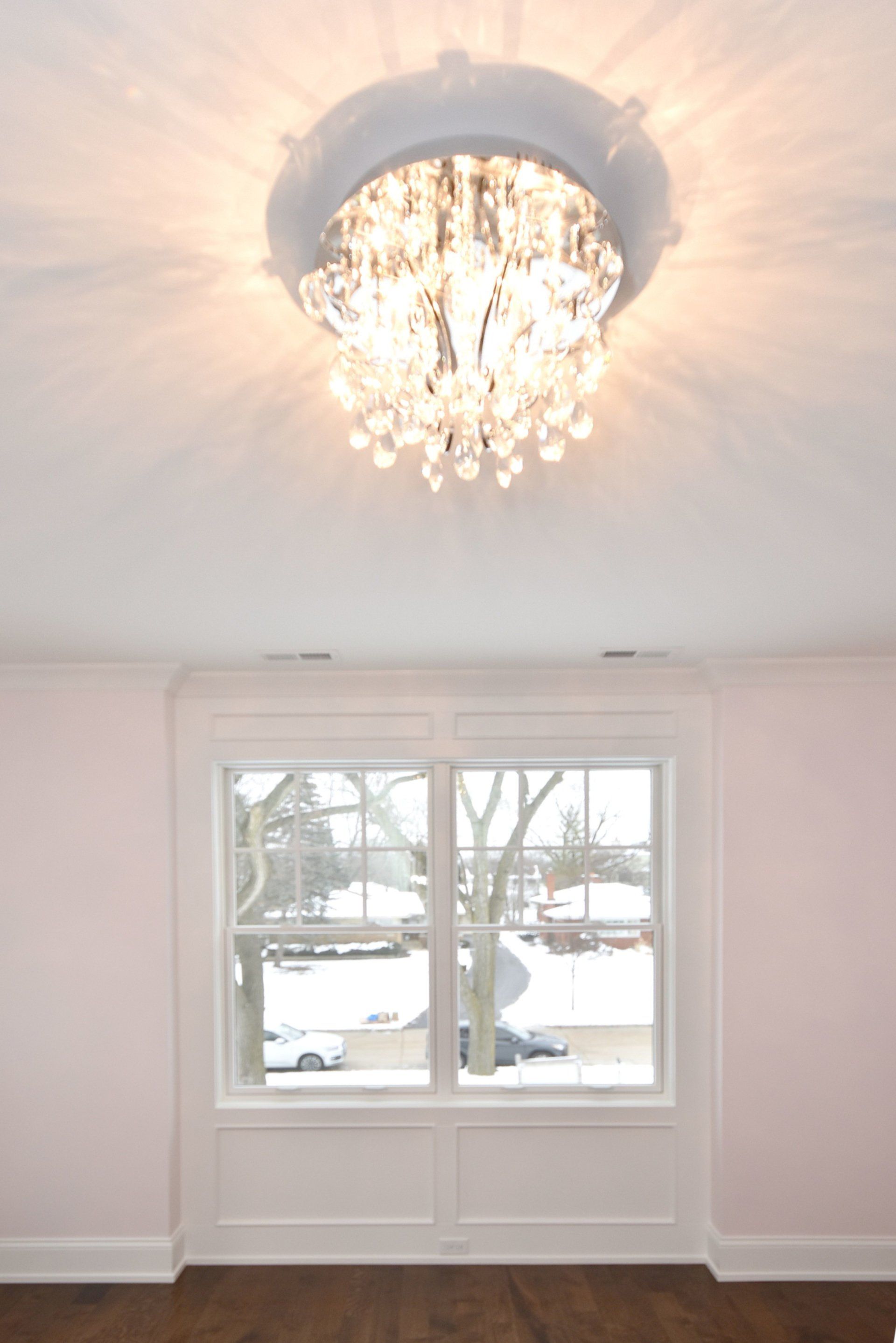 An empty room with a window and a chandelier hanging from the ceiling.