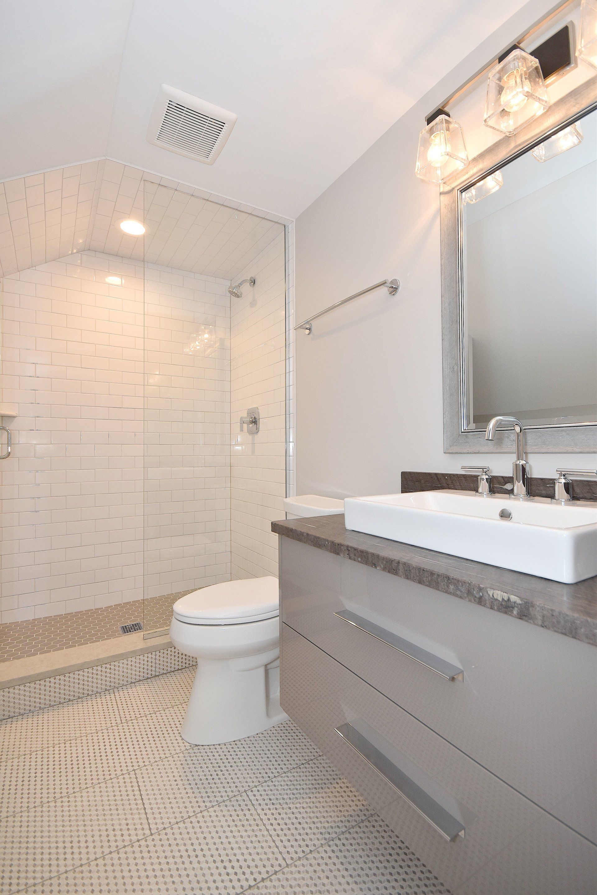 A bathroom with a toilet , sink , mirror and walk in shower.