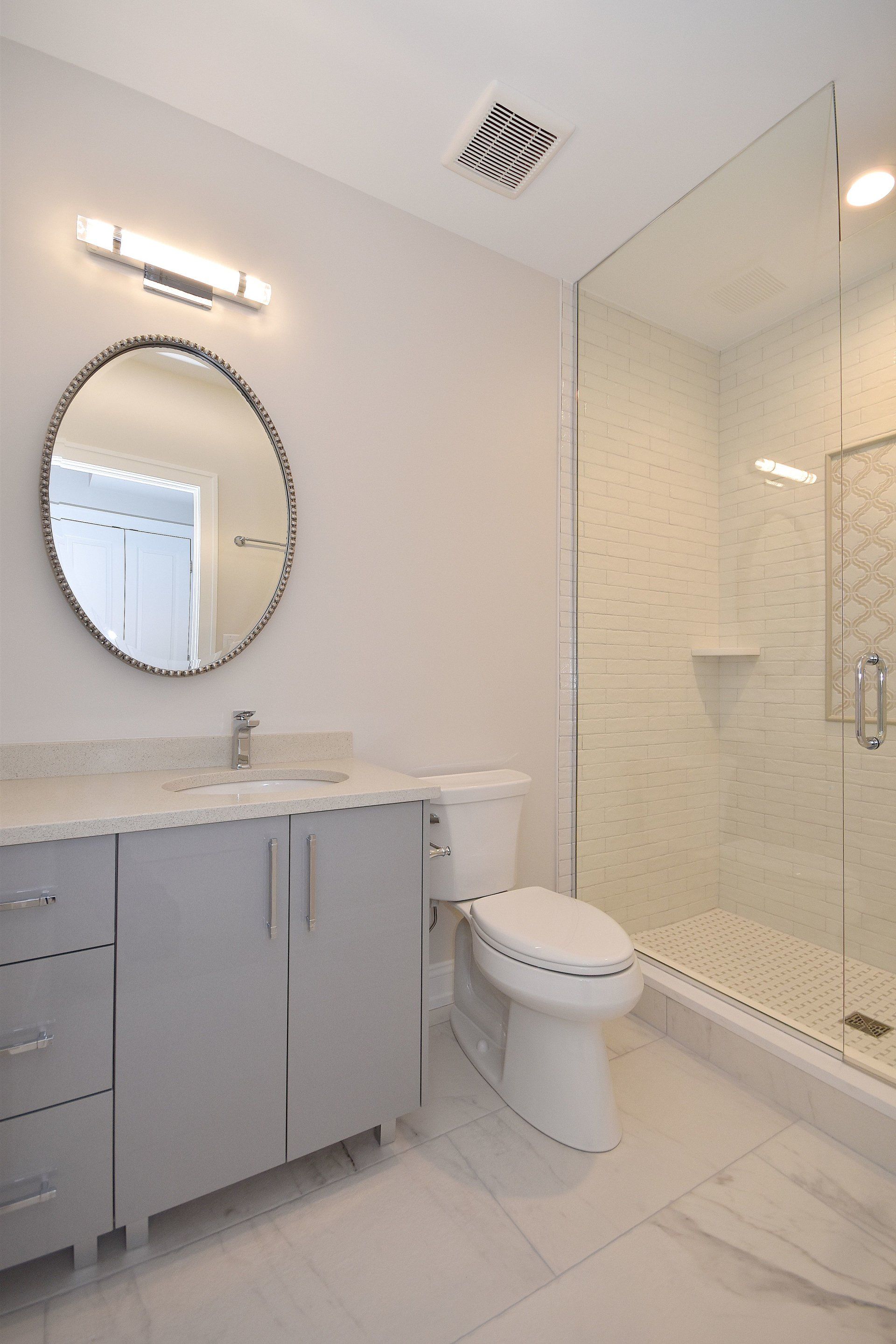 A bathroom with a toilet , sink , mirror and walk in shower.