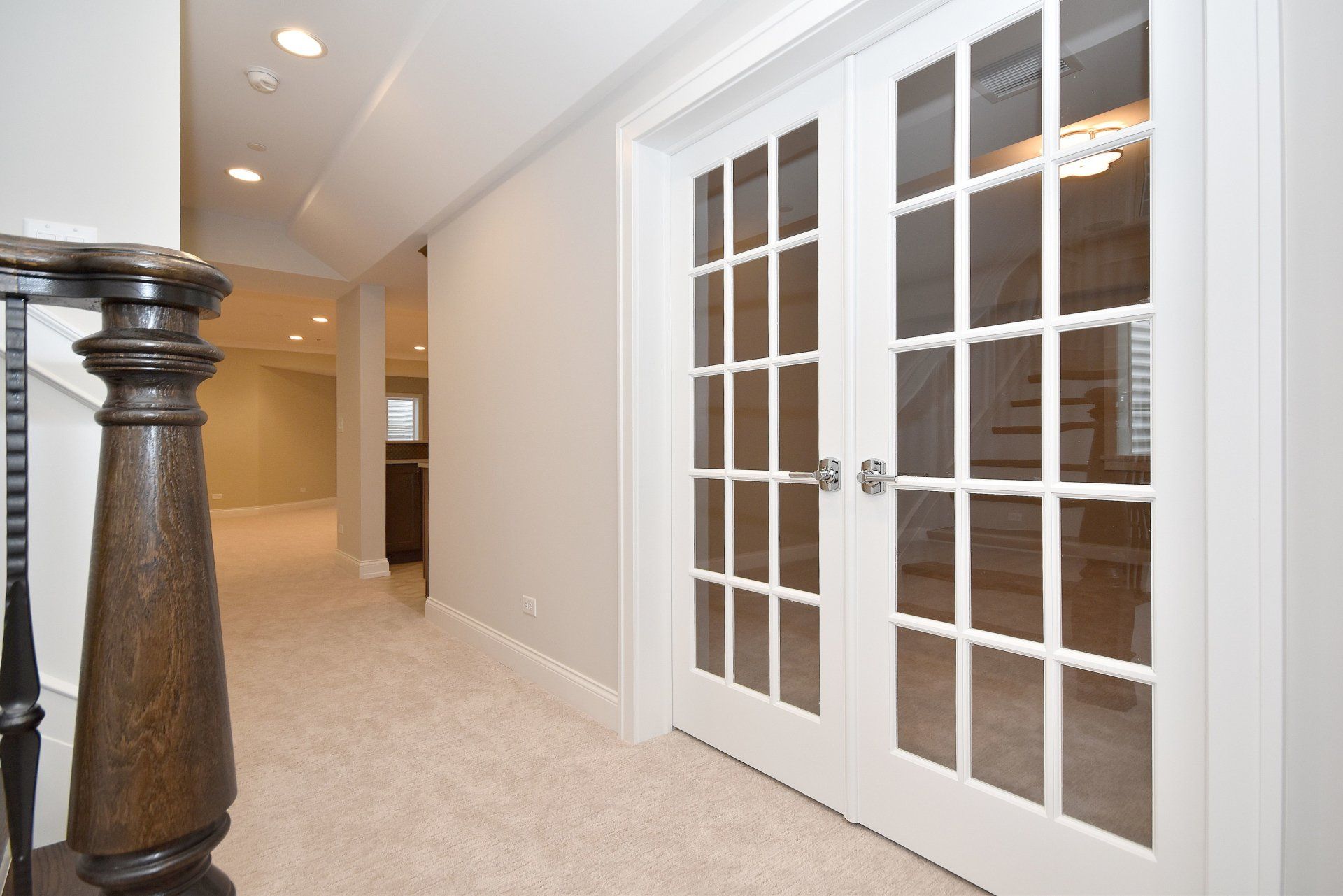 A hallway in a house with french doors and a wooden railing.