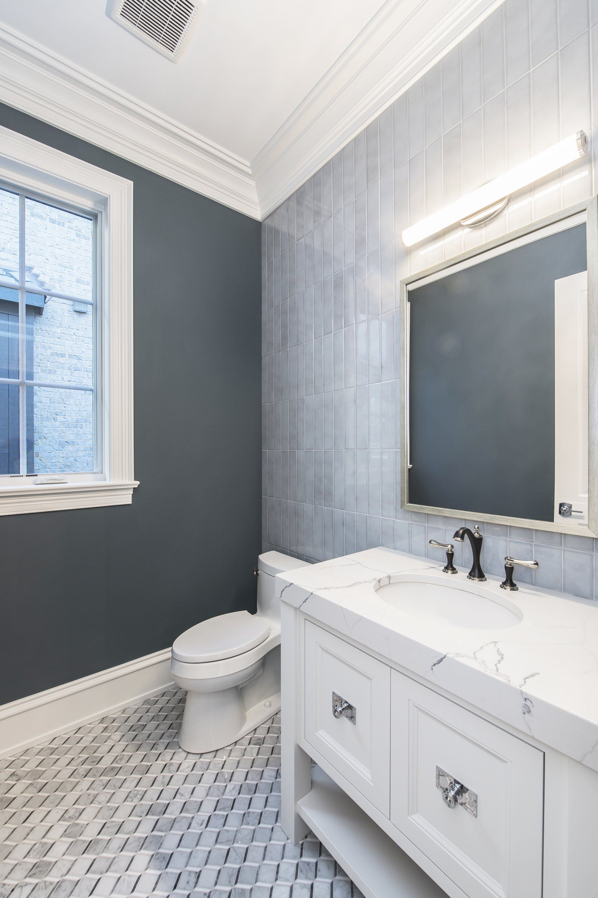 A bathroom with a toilet , sink , mirror and window.
