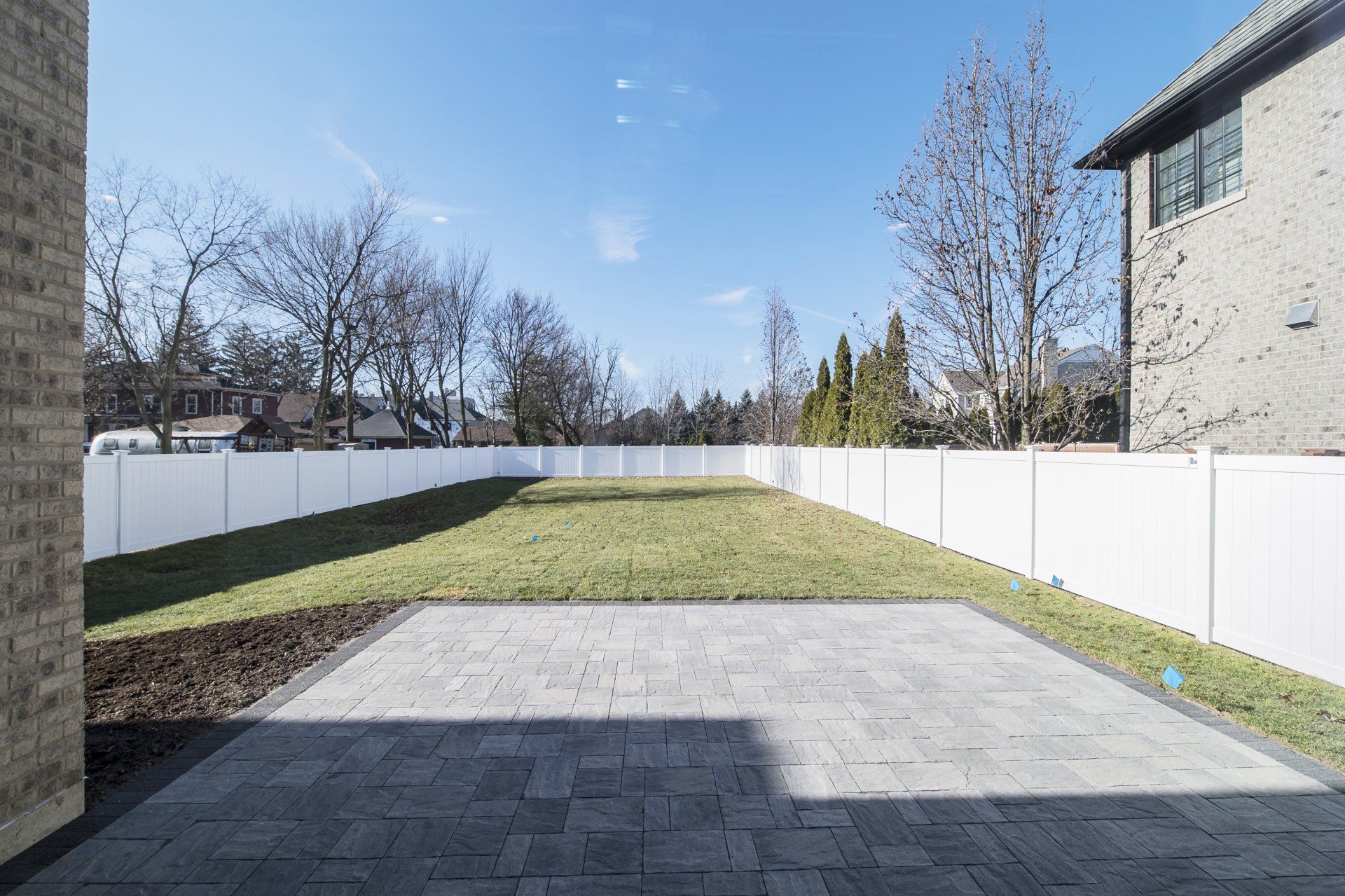 The backyard of a house with a large lawn and a white fence.