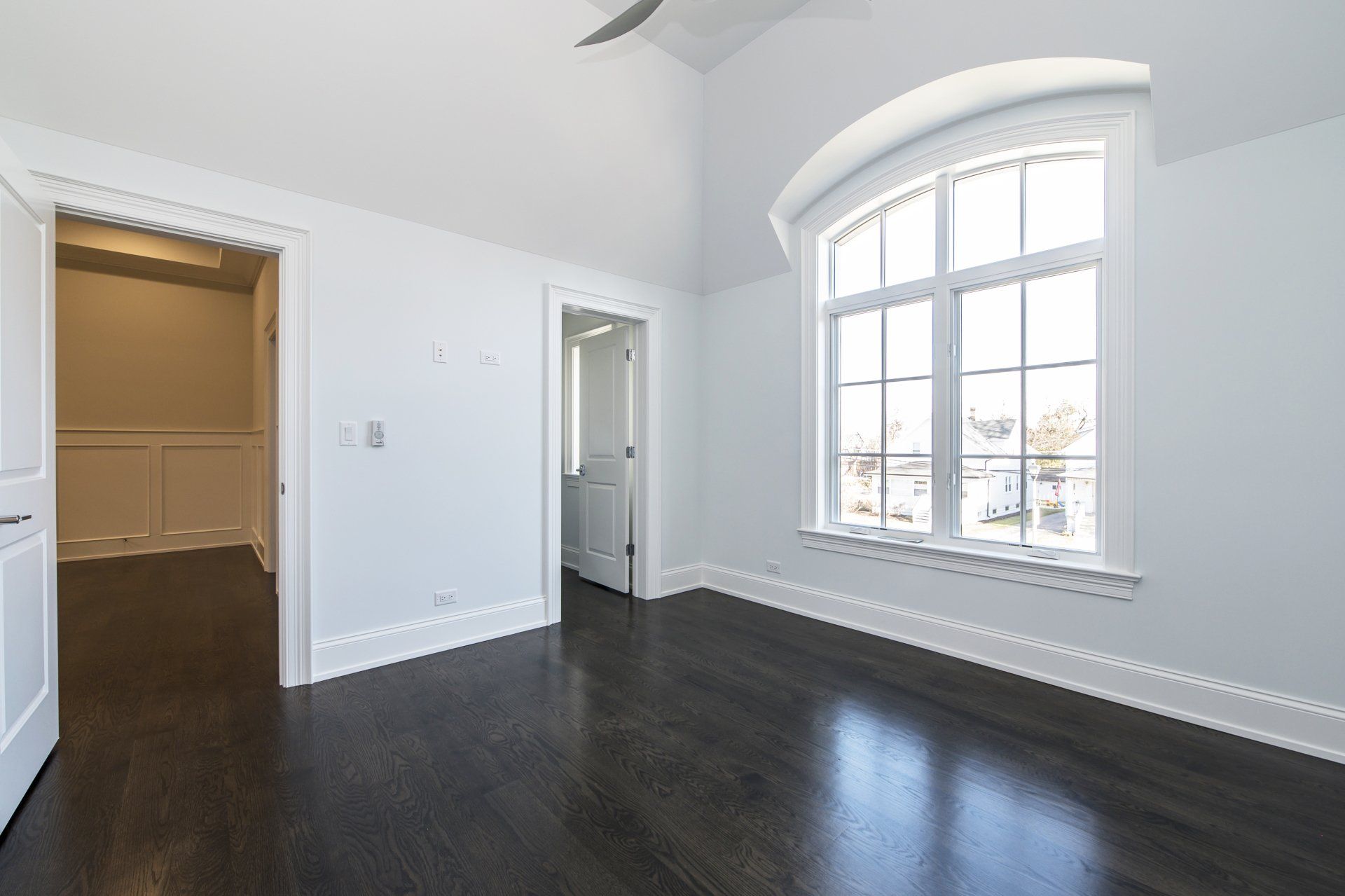 An empty room with a large window and a ceiling fan.