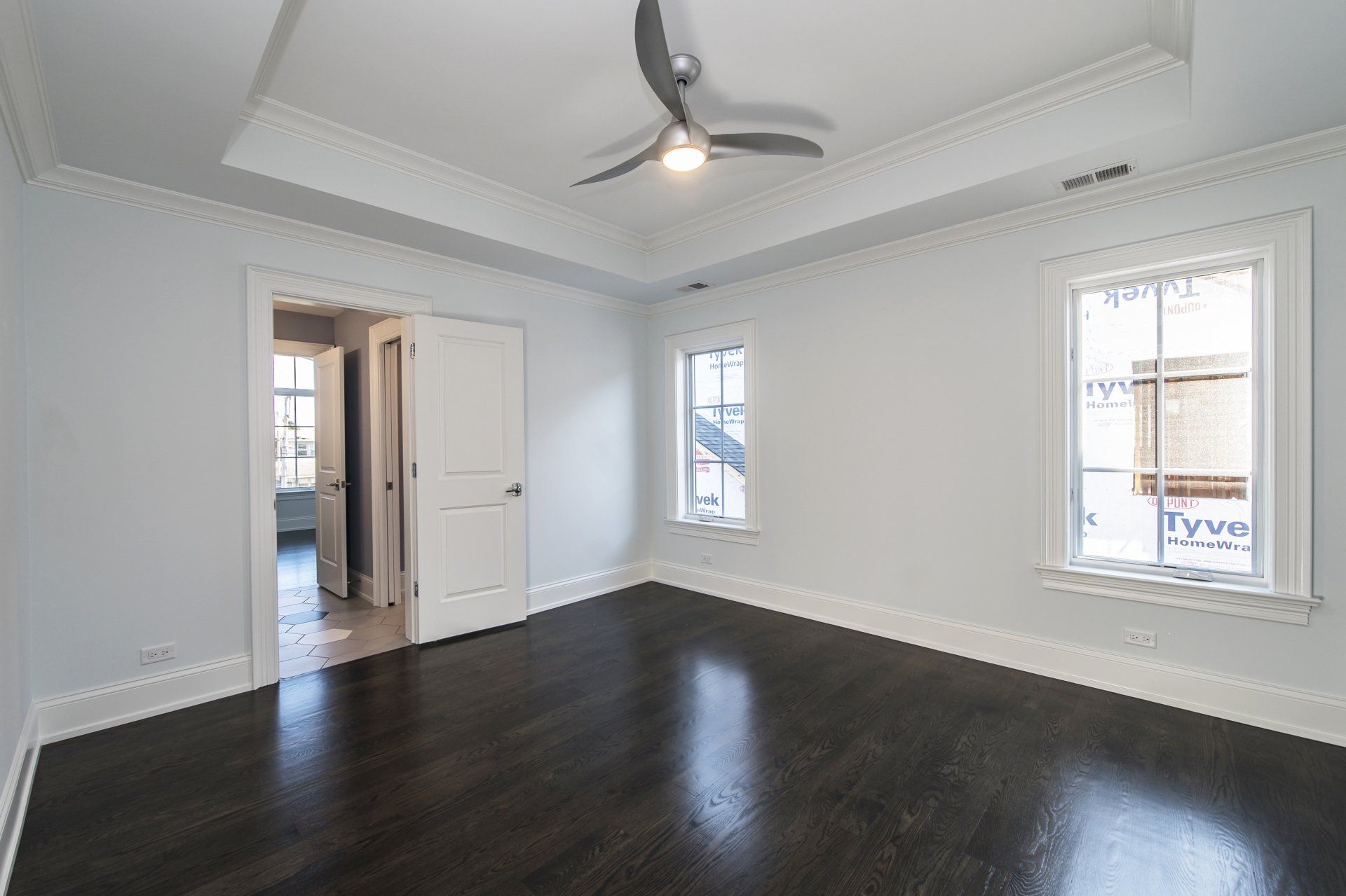 An empty room with a ceiling fan and two windows.