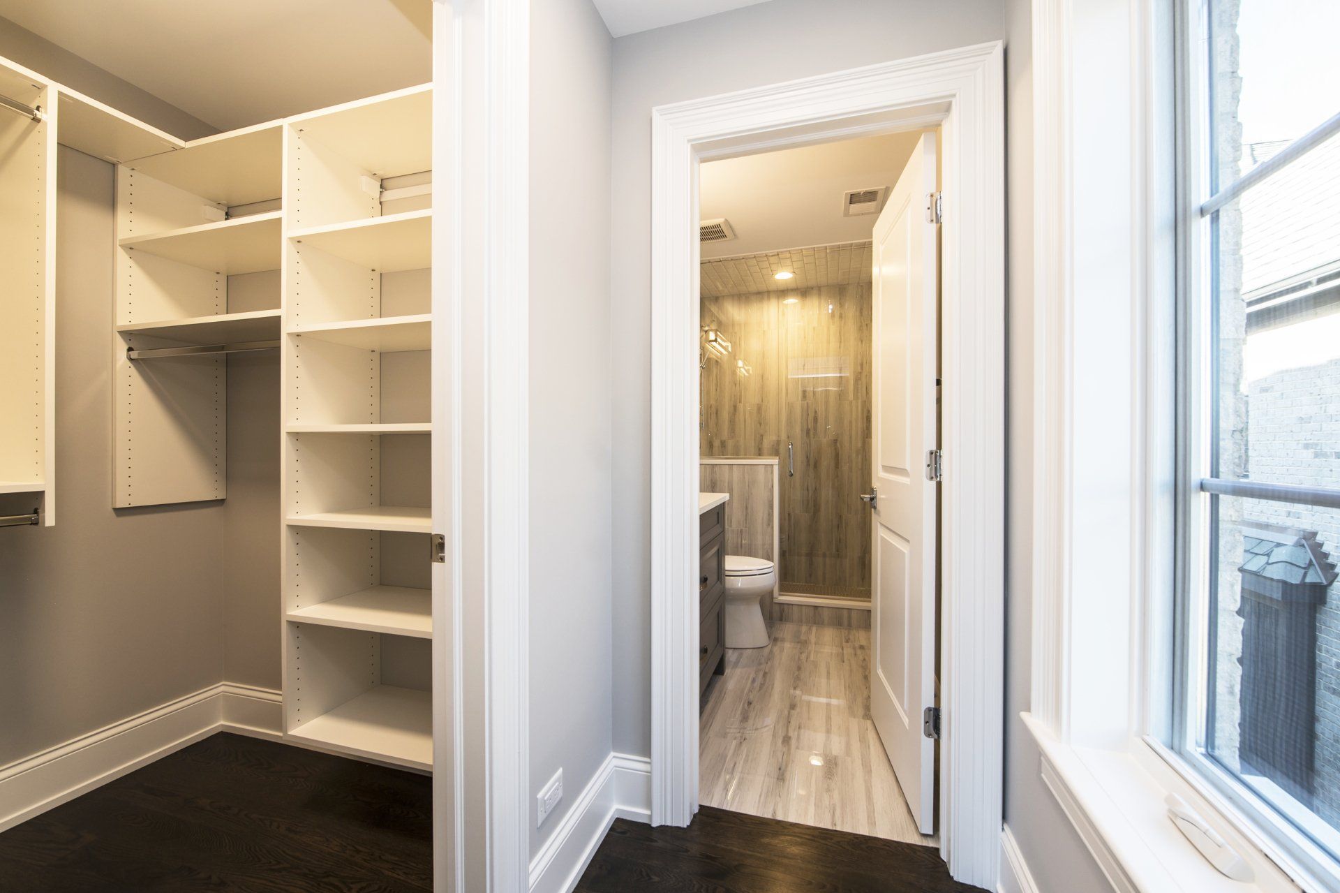 A walk in closet with shelves and a window leading to a bathroom.