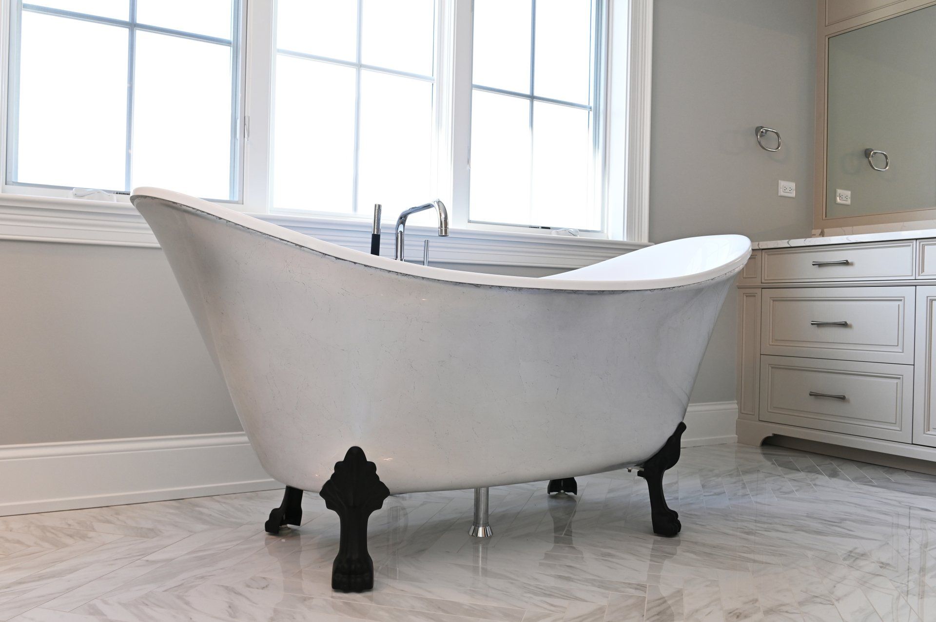 A white bathtub with black legs is in a bathroom next to a window.