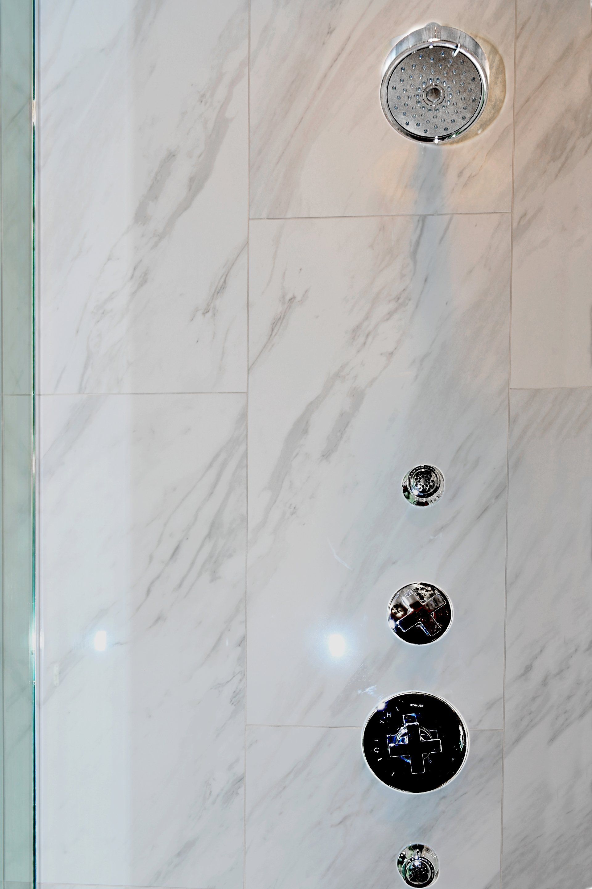 A close up of a shower head on a white tiled wall
