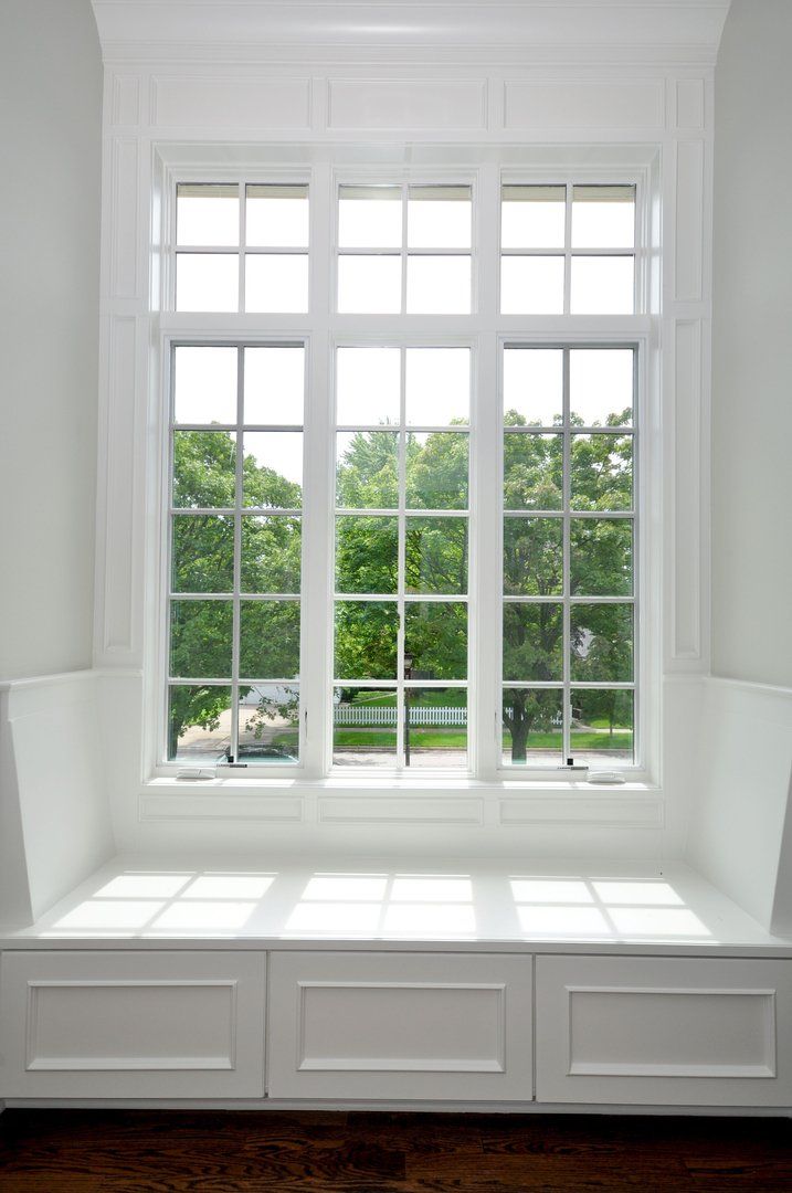 There is a window seat in front of a window with a view of trees.