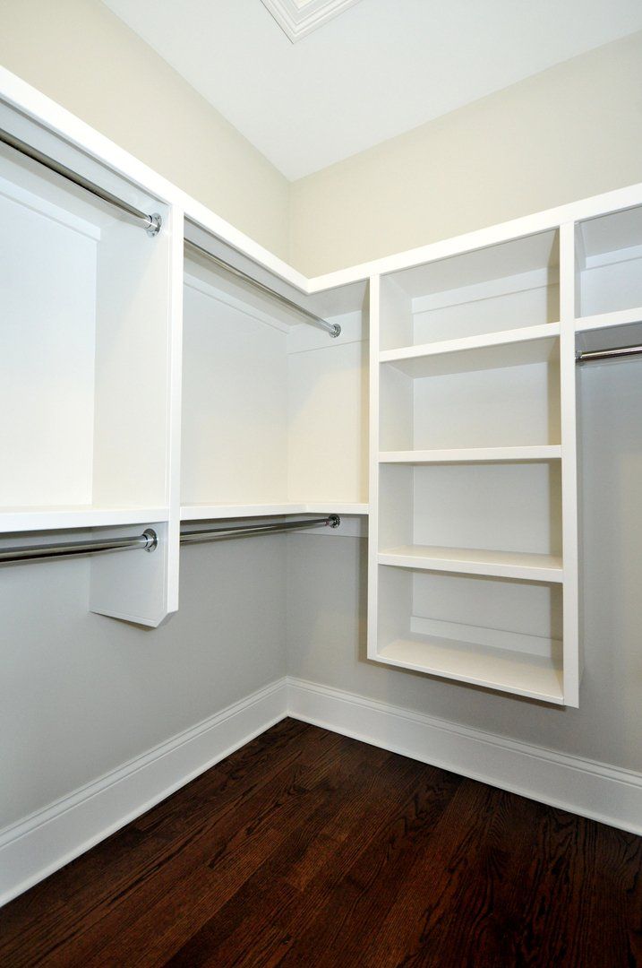 A walk in closet with wooden floors and white shelves.