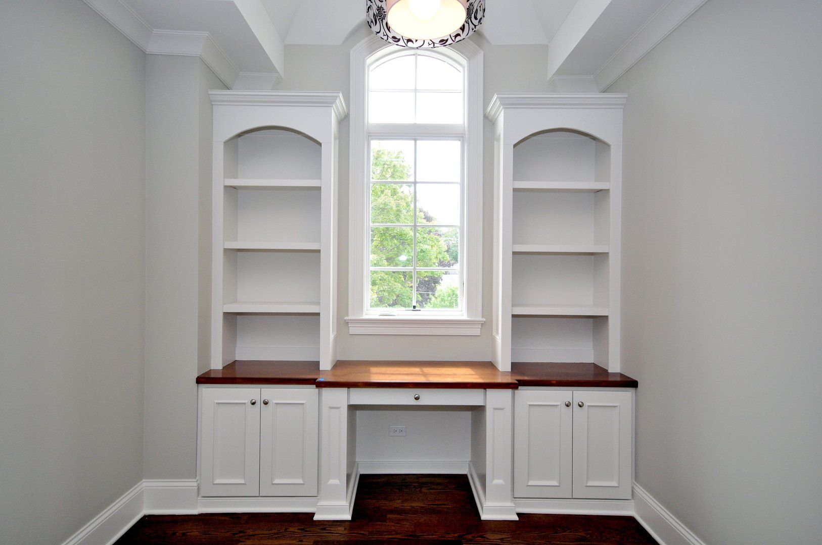An empty room with a desk , shelves and a window.