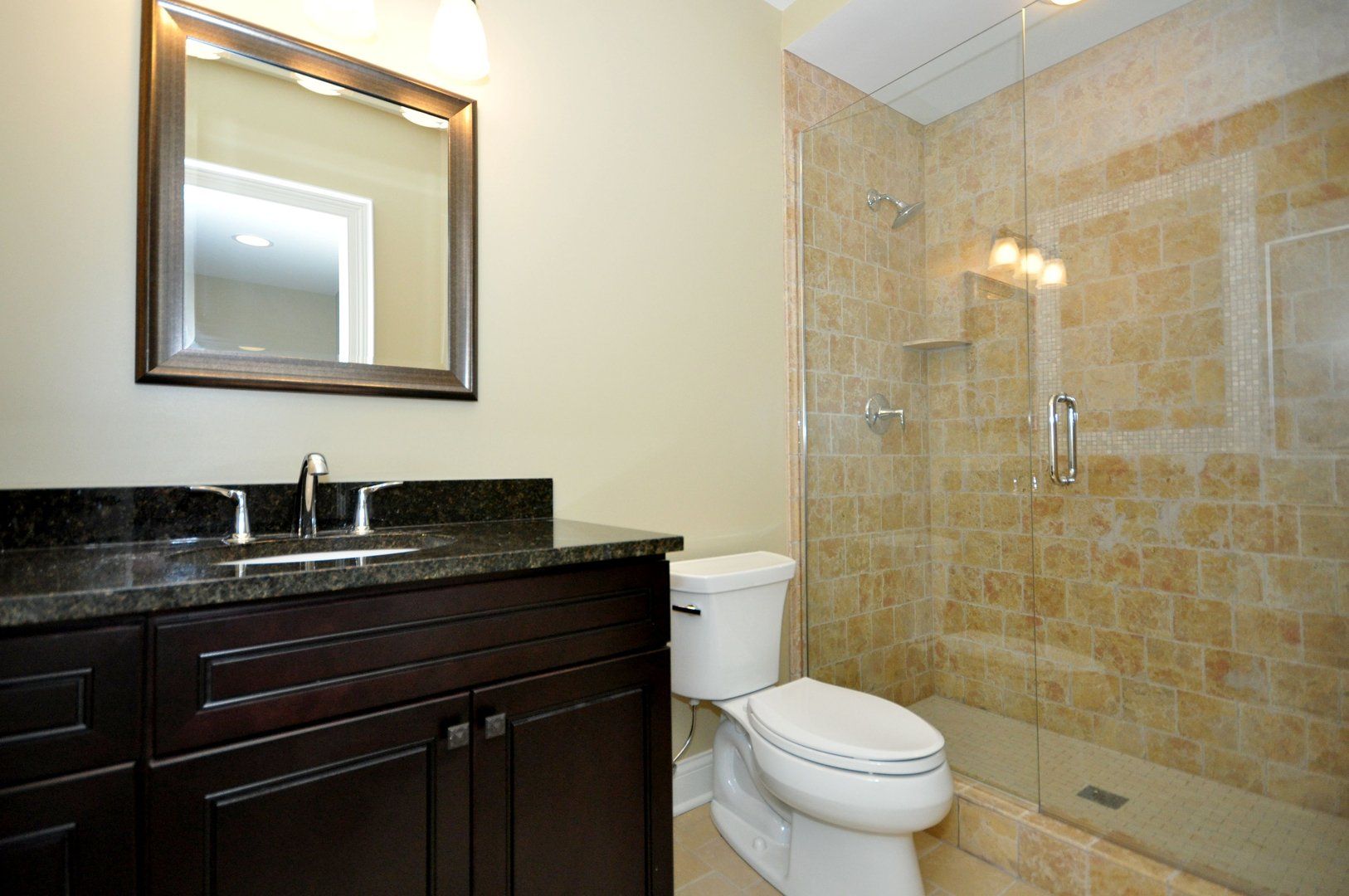 A bathroom with a toilet , sink , mirror and walk in shower.