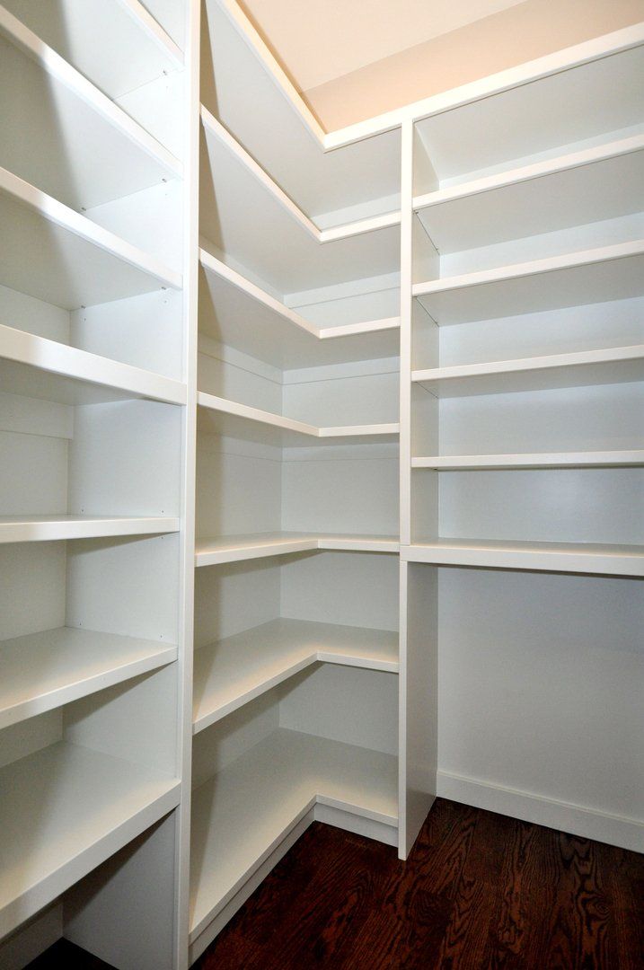 A walk in closet with lots of shelves and a wooden floor